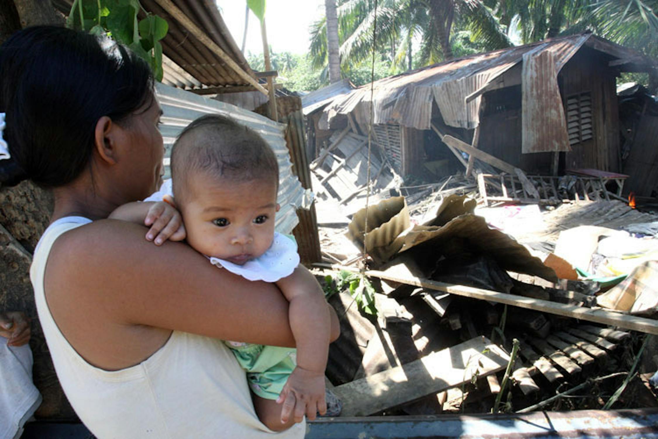 La piccola Marry, 4 mesi, in braccio alla mamma di fronte alle macerie della sua casa - ©UNICEF Filippine/2011/Maitem