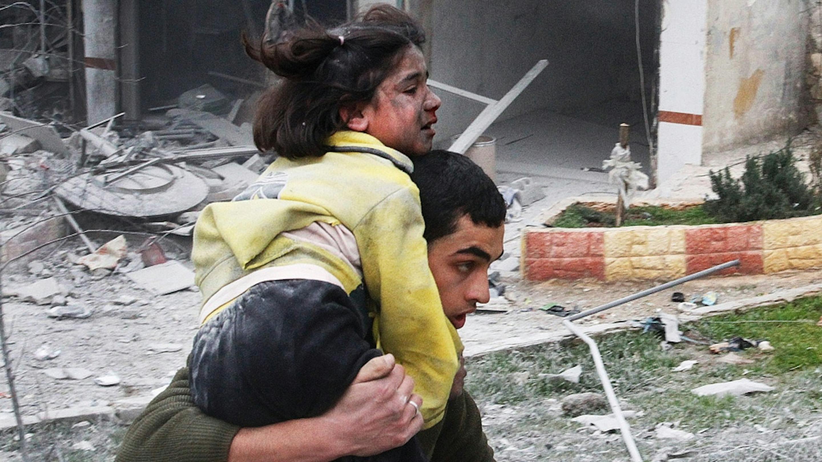 Un ragazzo trasporta la sorellina, ferita durante un bombardamento su Ansari, quartiere di Aleppo, febbraio 2013 - ©AP/Abdullah al-Yassin