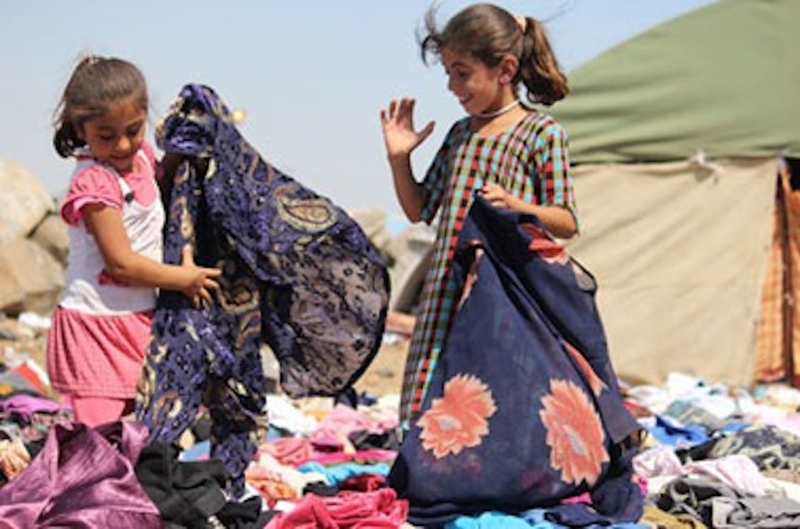 Due bambine rifugiate stanno setacciando tra mucchi di vestiti arrivati presso il campo Nawrouz, cercando di trovare le taglie adatte a loro. ©UNICEF/Syria-2014/Rashidi