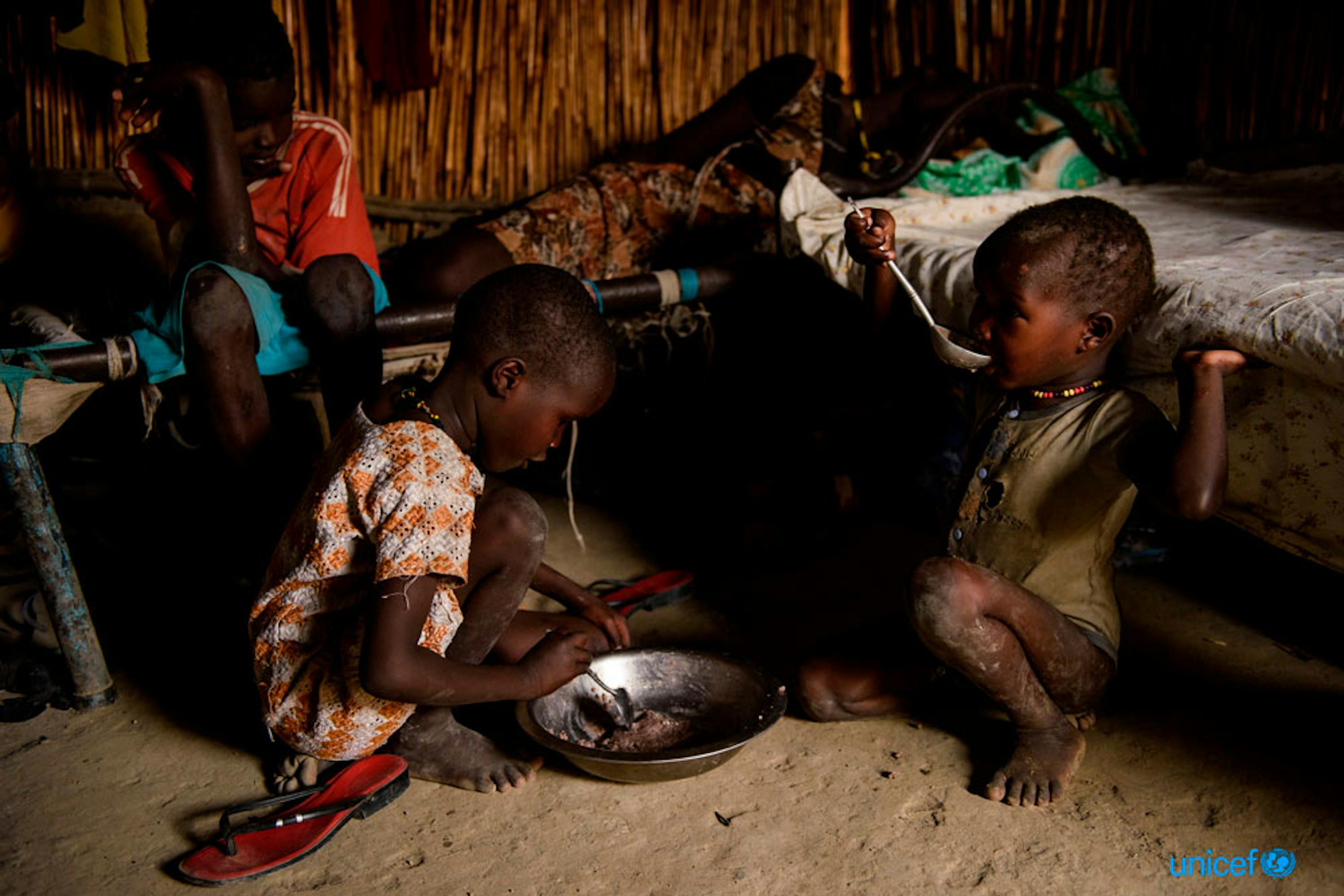 Nyakuma Chol di 7 anni e Nyeyang Chol di 4, mangiano un piatto  di porridge e sorgo nella loro stanza condivisa con altre famiglie sfollate all'interno del sito di protezione dei civili di Bentiu, Sud Sudan - © UNICEF/UN070626/Hatcher-Moore