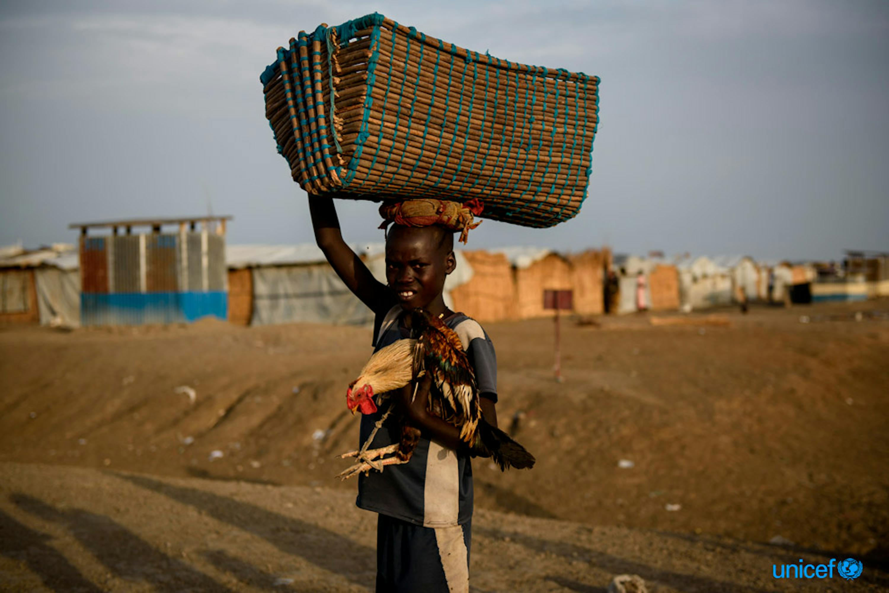 Latjor Mayal di 12 anni porta con se, nel sito di protezione dei civili di Bentiu in Sud Sudan, un cesto di oggetti e un pollo - © UNICEF/UN070627/Hatcher-Moore