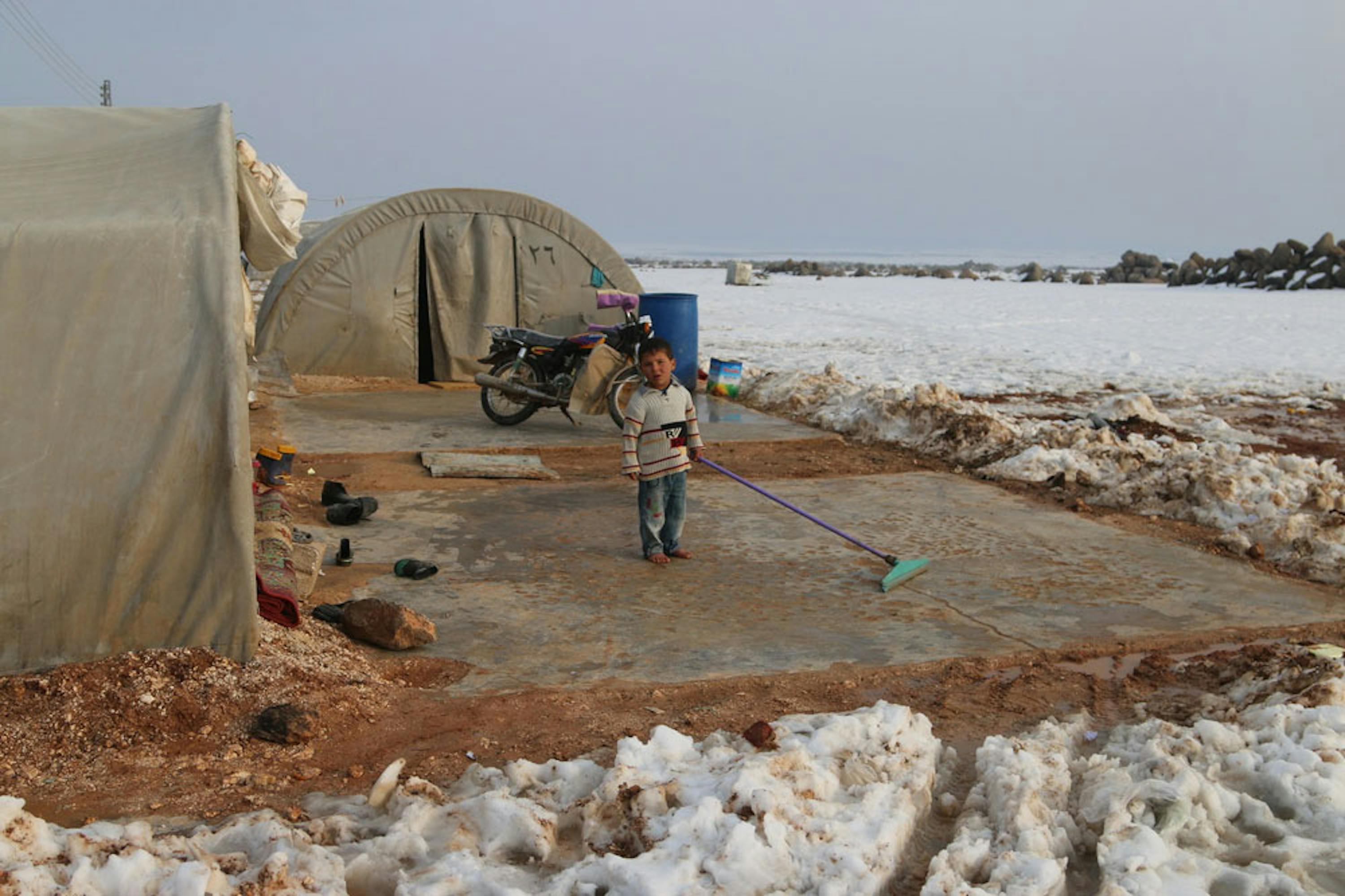 Un bambino spala la neve davanti alla tenda nel campo per sfollati al-Nour, nei dintorni della città siriana di Idlib - ©UNICEF/UN046838/Alwan