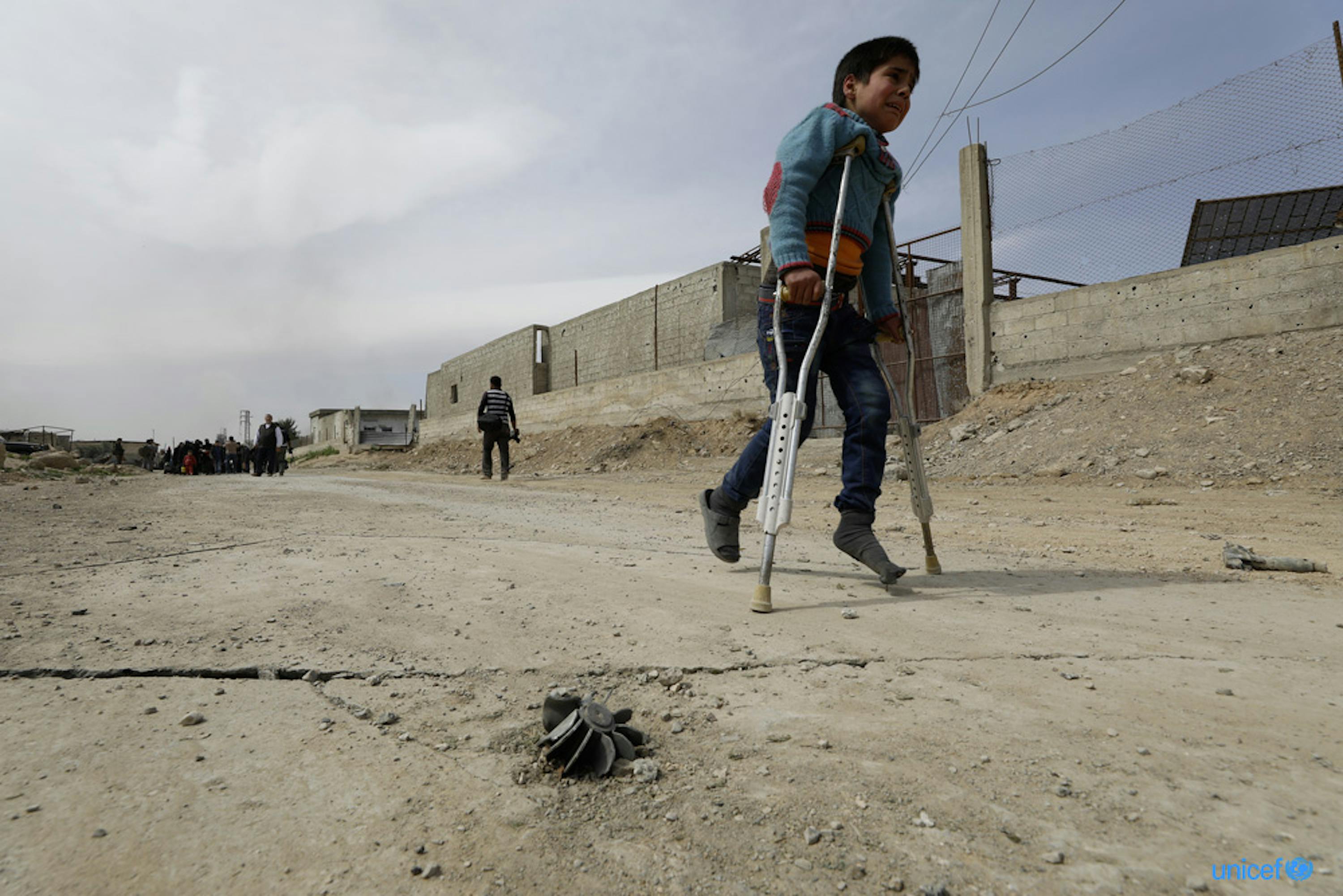 Un bambino ferito cammina con le stampelle verso la zona di evacuazione di Hamuriesh. Siria - © UNICEF/UN0185403/Sanadiki