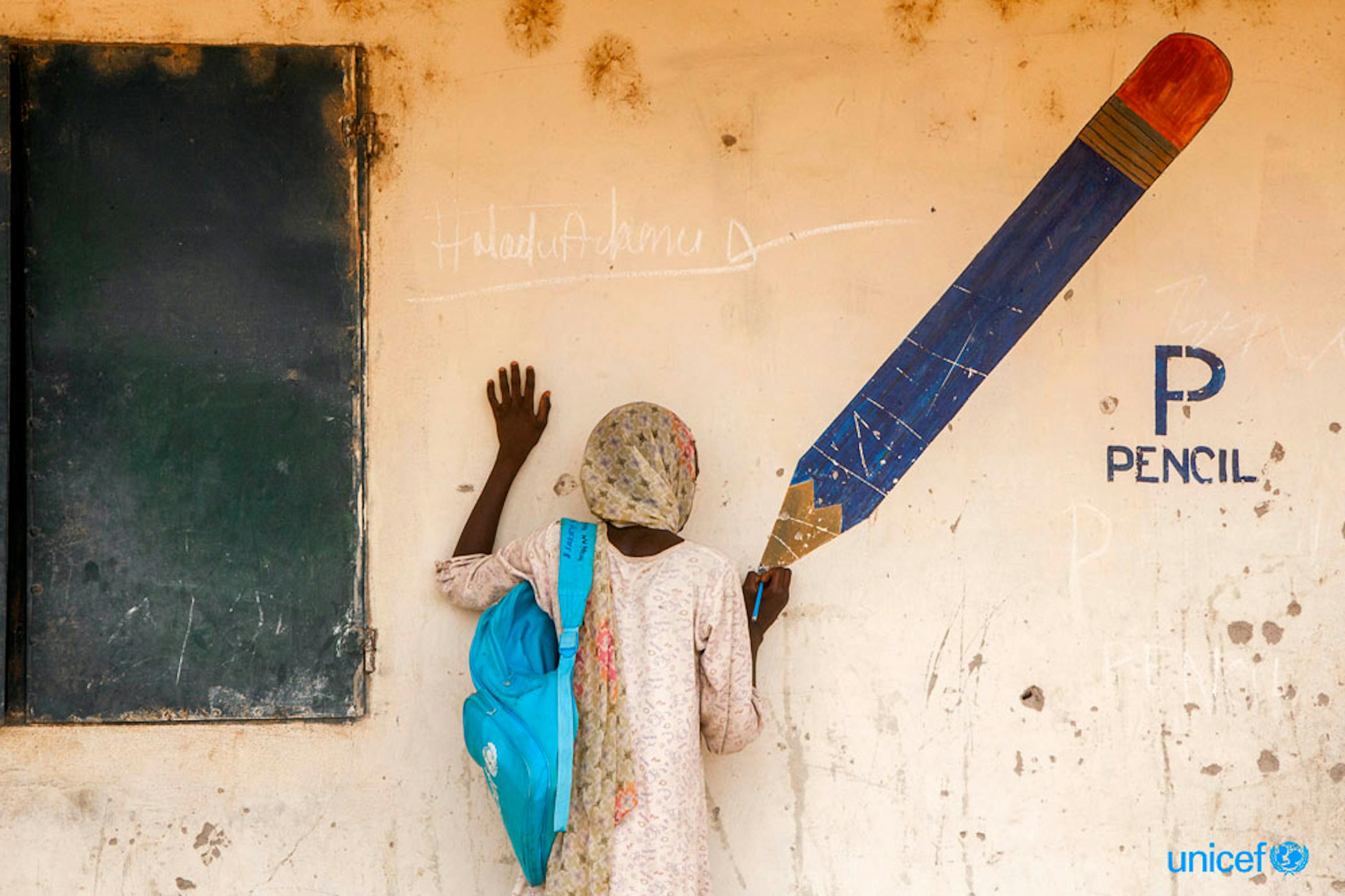 Aisha, 13 anni, finge di disegnare sulla punta di una matita dipinta su un murale in un campo per sfollati nello stato di Adamawa, in Nigeria. © UNICEF/UNI181410/Esiebo