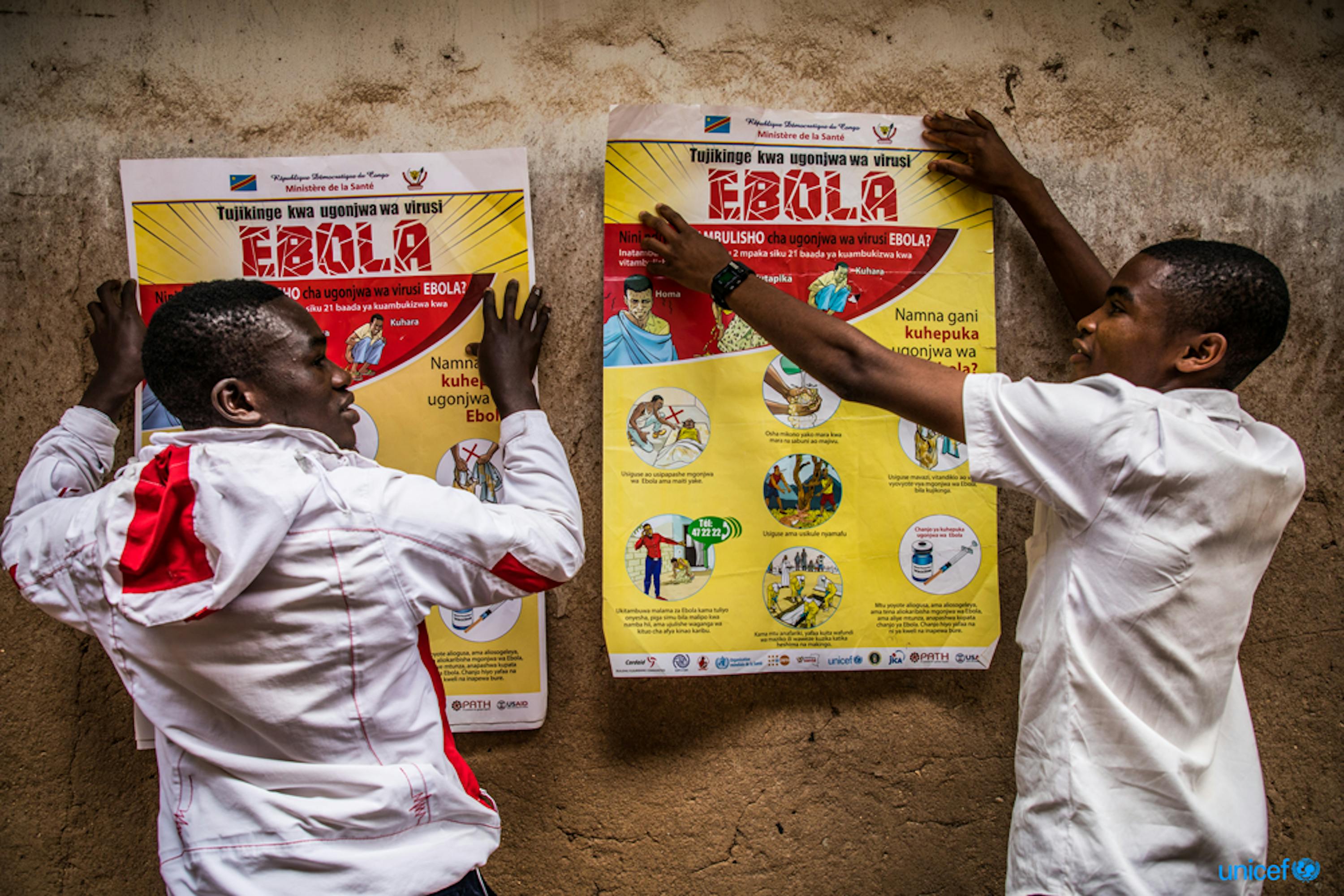 Congo. due studenti affissano alla parete della loro scuola un poster che descrive la sensibilizzazione all'ebola  © UNICEF/UN0311511/Tremeau