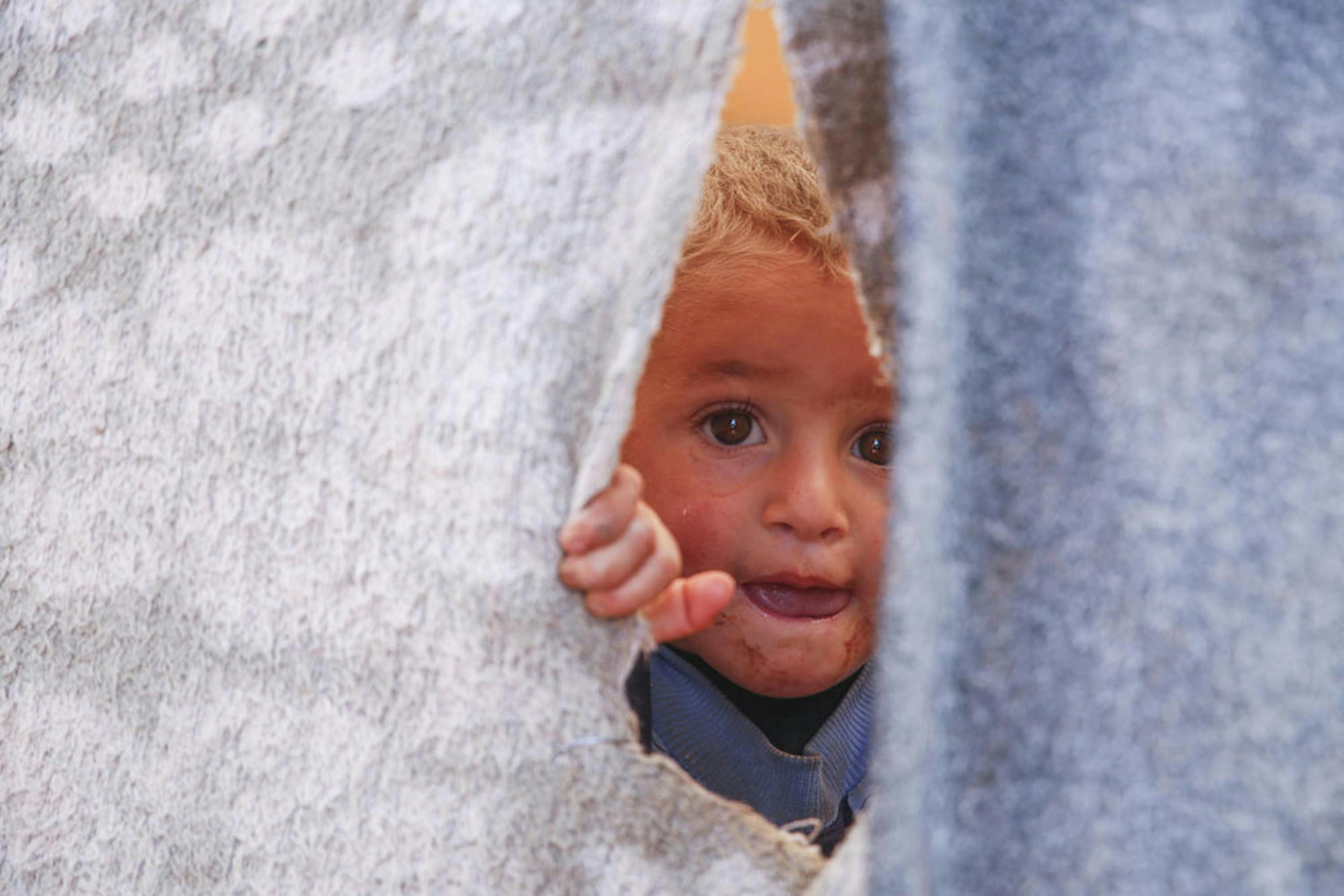 Un bambino sbircia da una tenda nel campo per sfollati di Killi, al confine tra Siria e Turchia. La sua famiglia è fuggita da Idlib, teatro di aspri combattimenti - © UNICEF/UN0348583/Saad