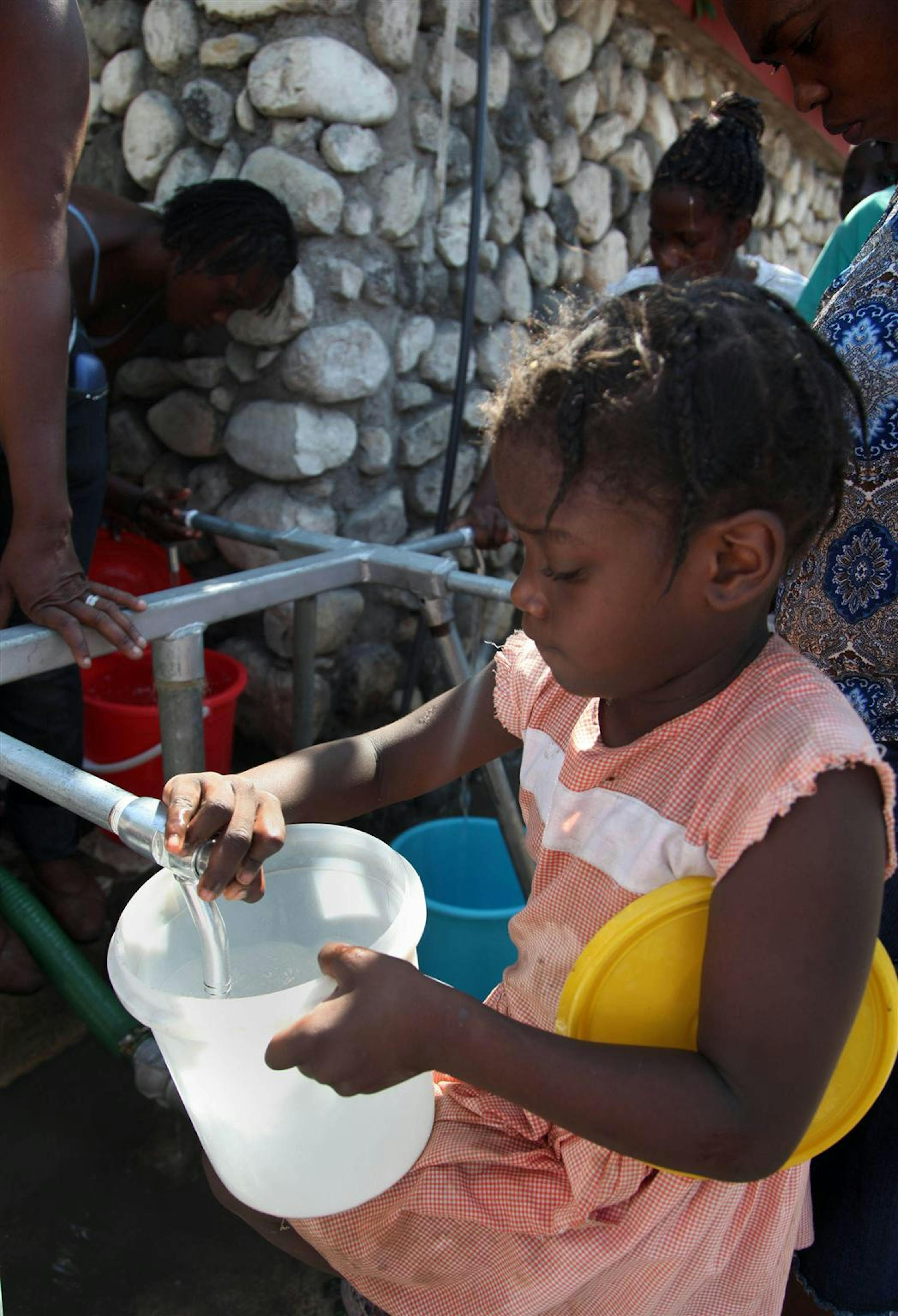 Una bambina attinge acqua da una cisterna installata dall'UNICEF nella piazza Champs-de-Mars, di fronte alle macerie del Palazzo presidenziale, dove si sono accampati 50.000 senzatetto