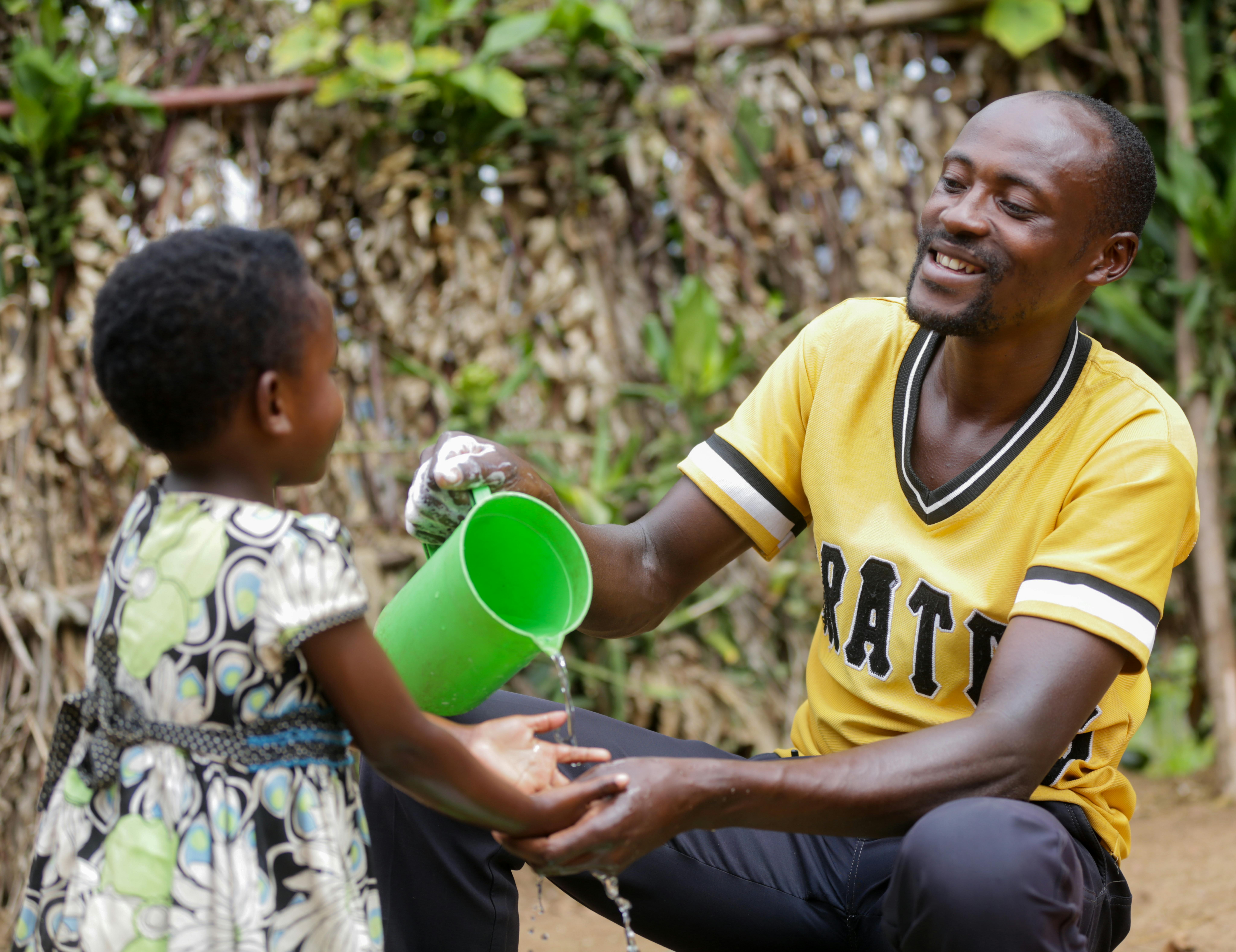 Ruanda, Natasha, tre anni, si lava le mani aiutata dal papà Jean Bosco Ndayambaje.
