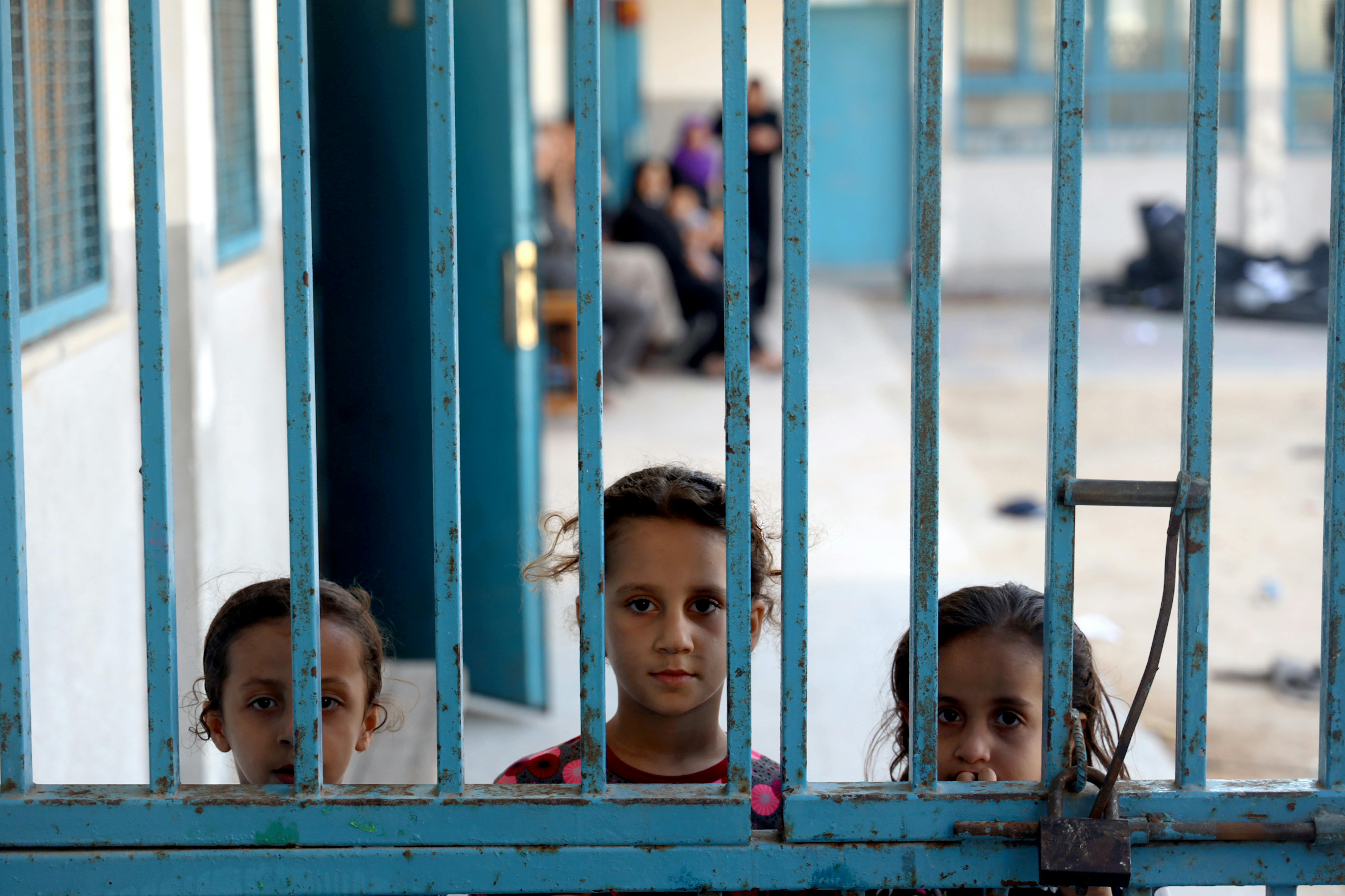 Tre bambine a Gaza guardano da un cancello di una delle 29 scuole dell'UNRWA usate come rifugio a causa dei pesanti bombardamenti.