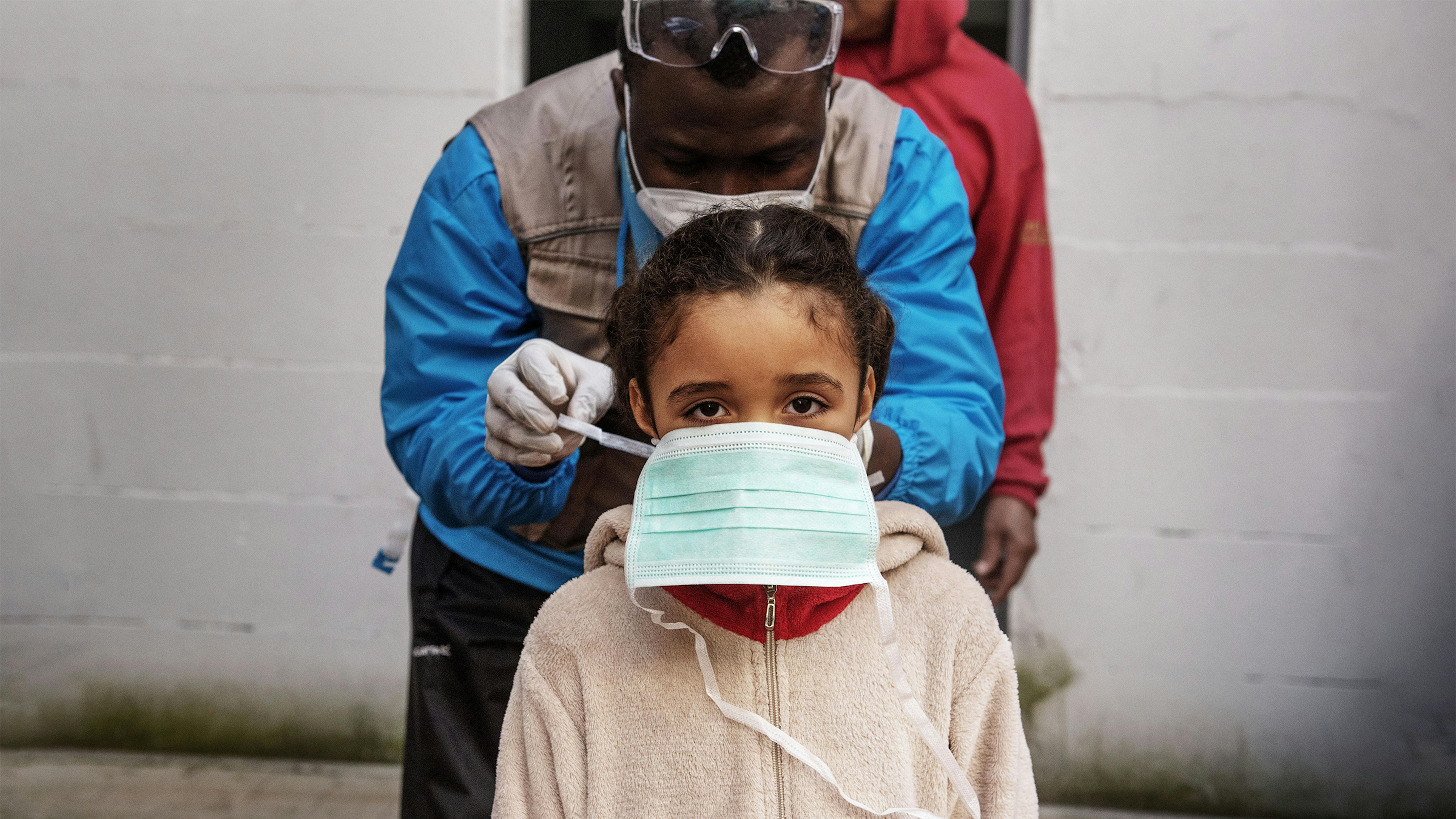 na bambina aiutata con una mascherina protettiva