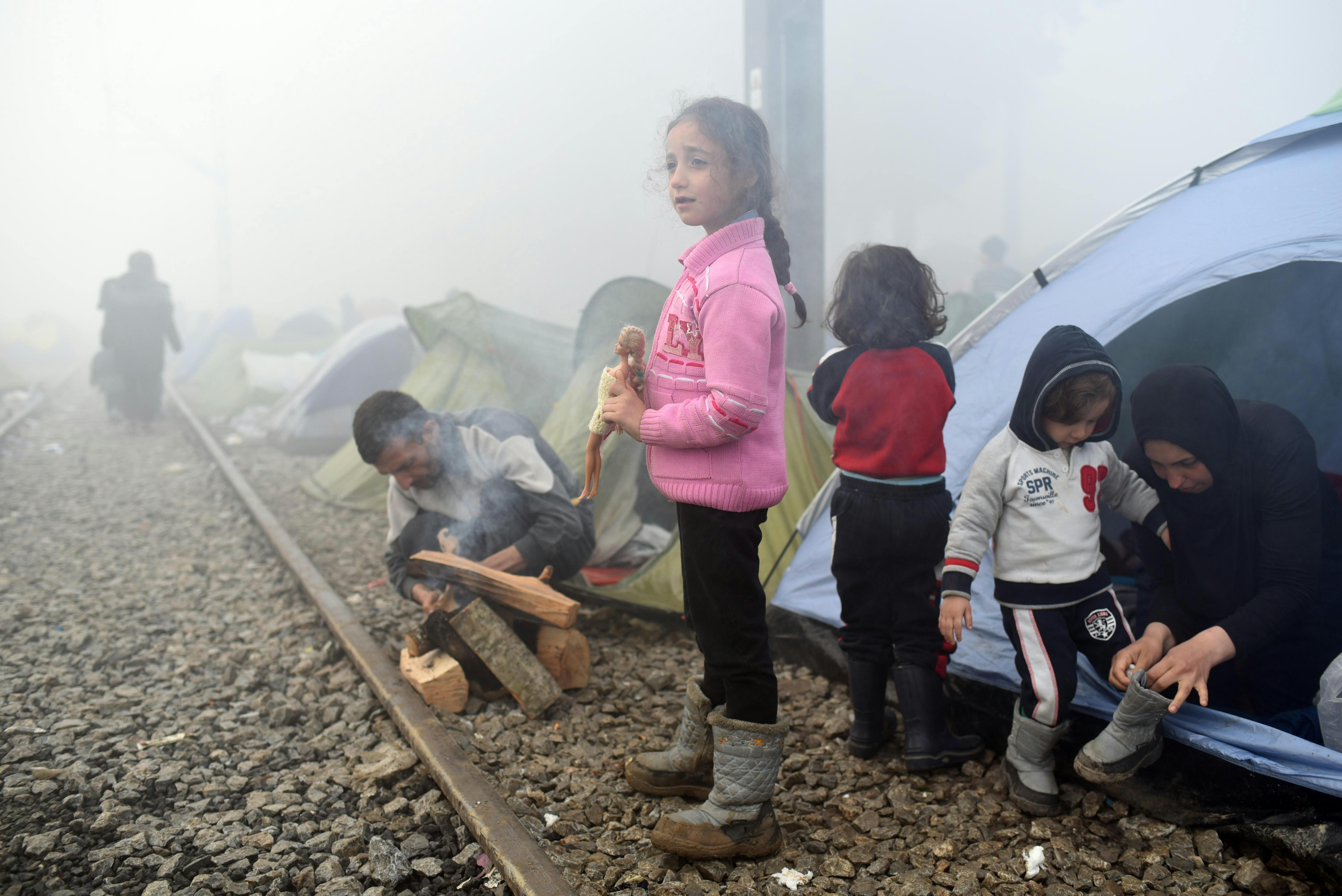 Grecia, una bambina tiene la sua bambola fuori da una fila di tende montate sui binari del treno. Siamo ad Idomeni