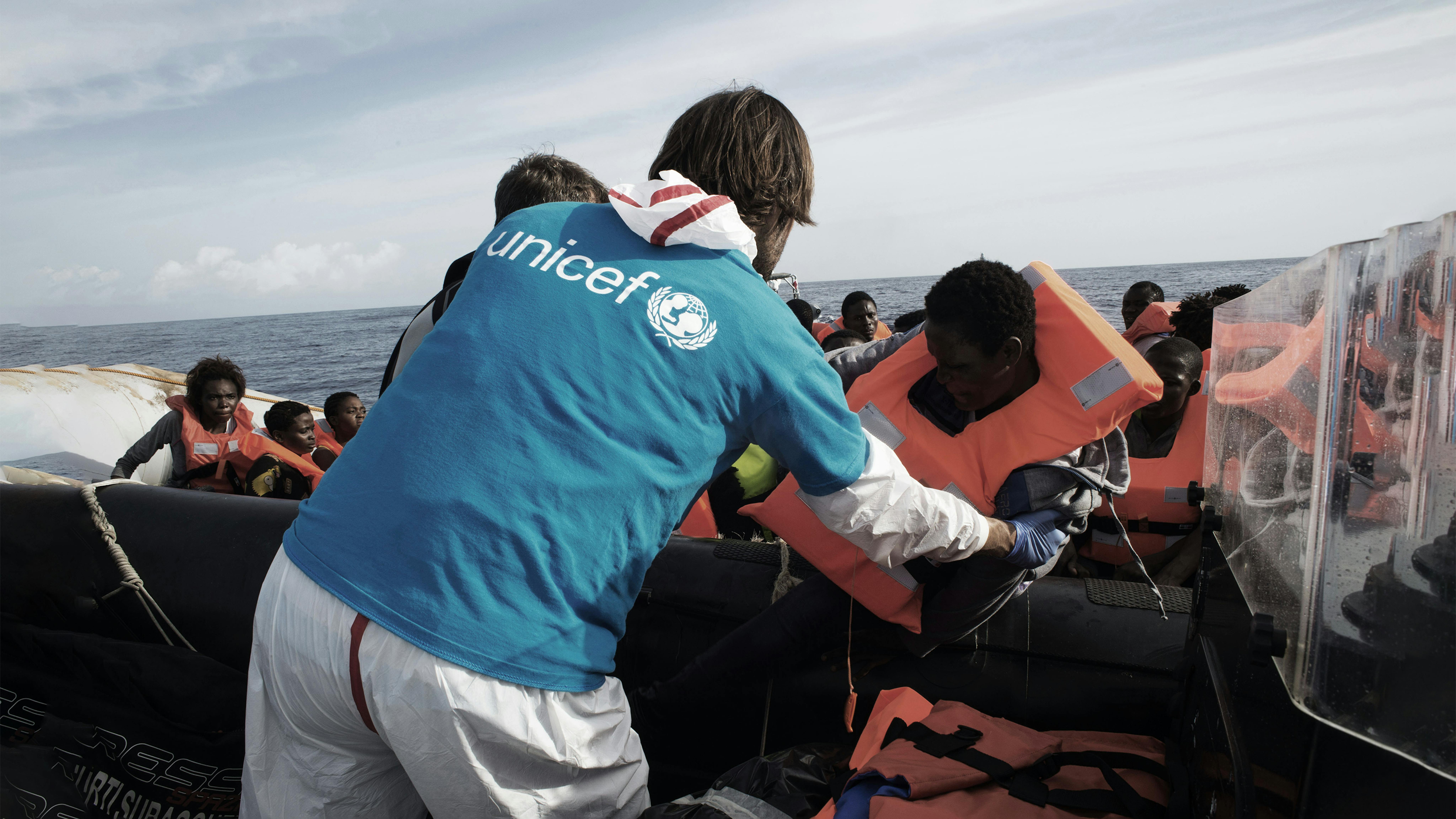 Un volontario italiano aiutare i migranti a trasferirsi dal gommone alla nave Fasan della Marina Militare