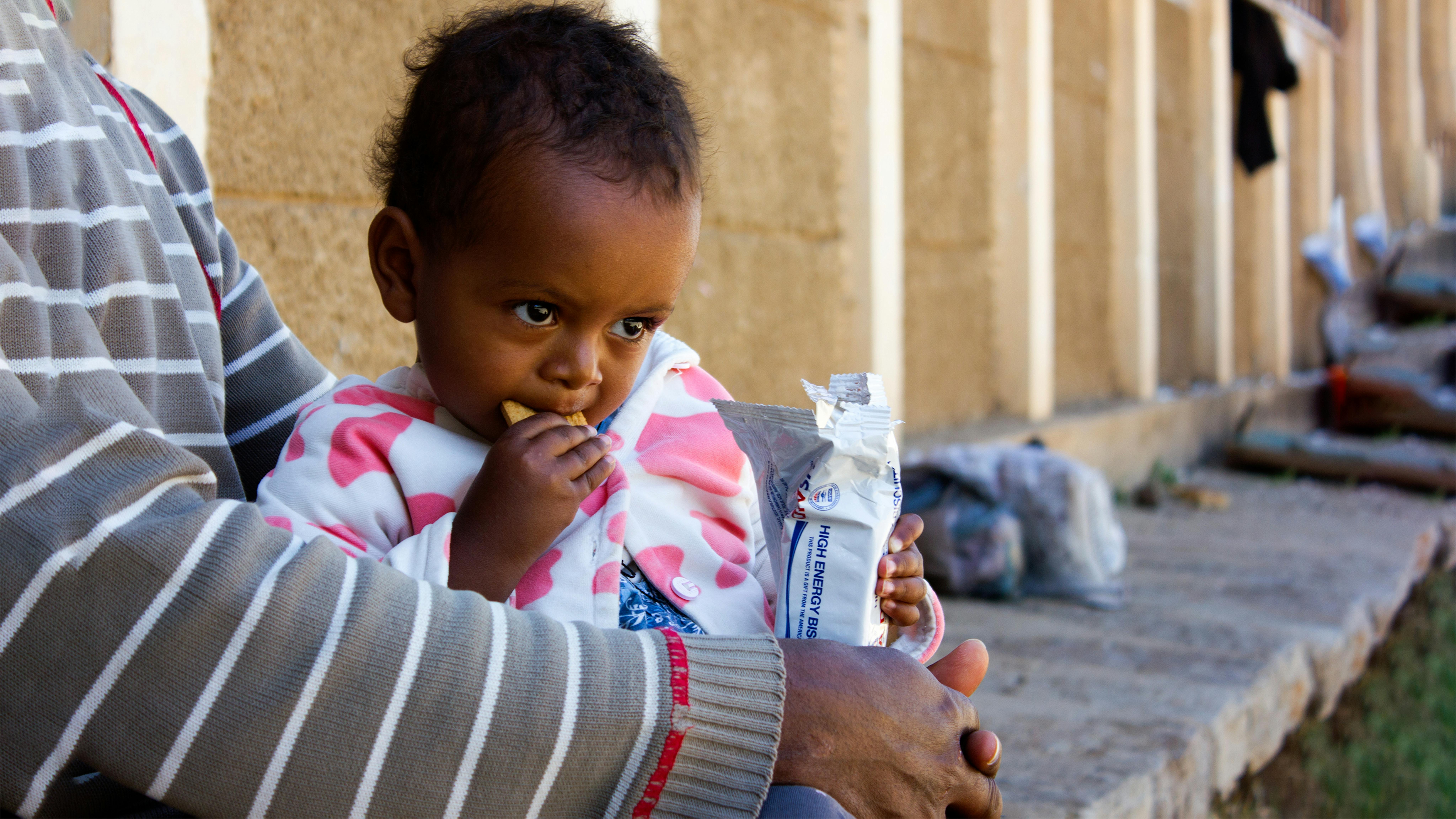 Etiopia, Meklit Desta,2, sta mangiando un biscotto ad alto contenuto energetico per aumentare i suoi livelli nutrizionali in un campo improvvisato a Mekelle