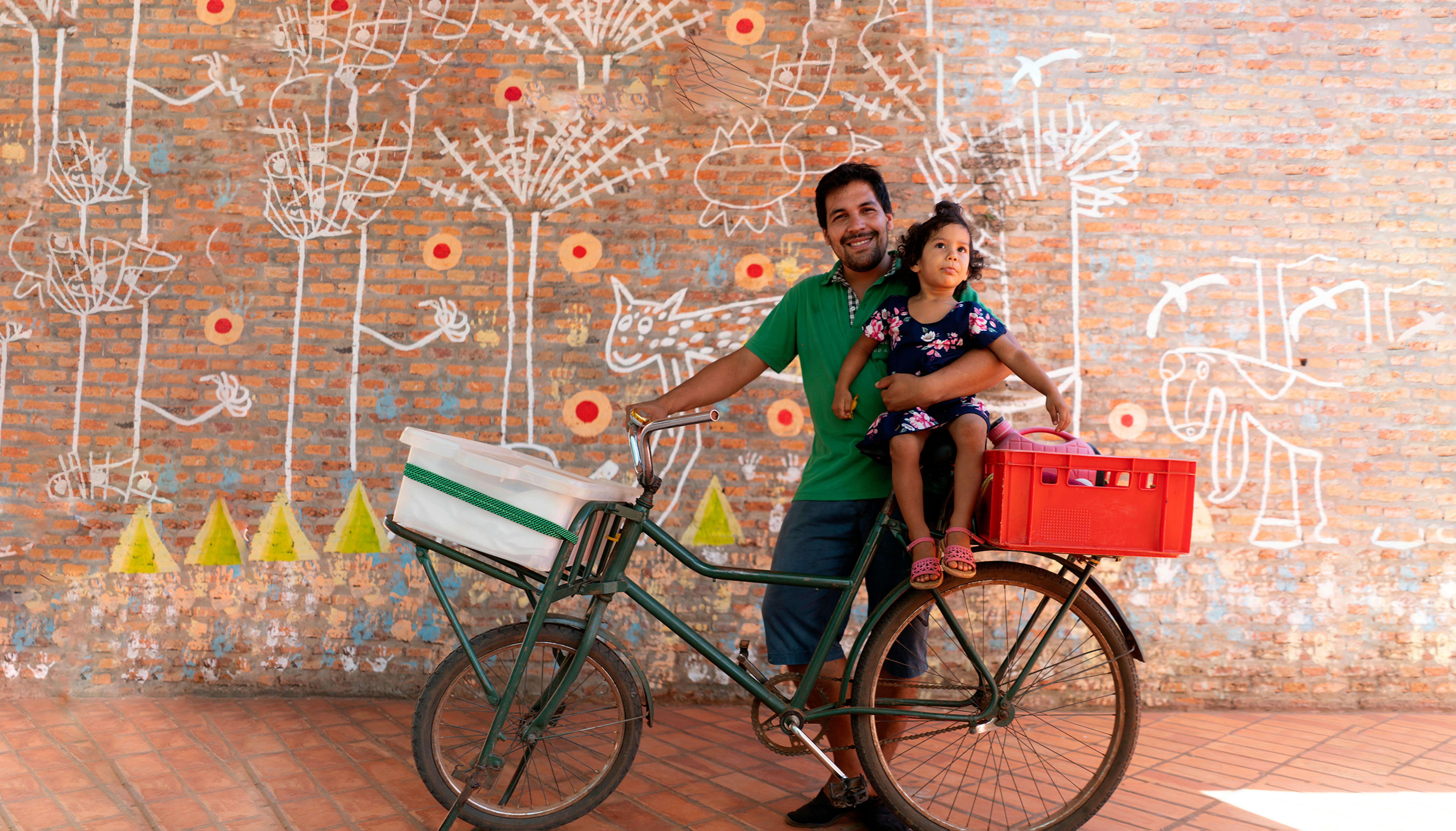 Paraguay. Rafael tiene in braccio sua figlia , 2 anni, seduta sulla bici che lui e sua moglie utilizzano per spostarsi e per consegnare il pane a lavoro