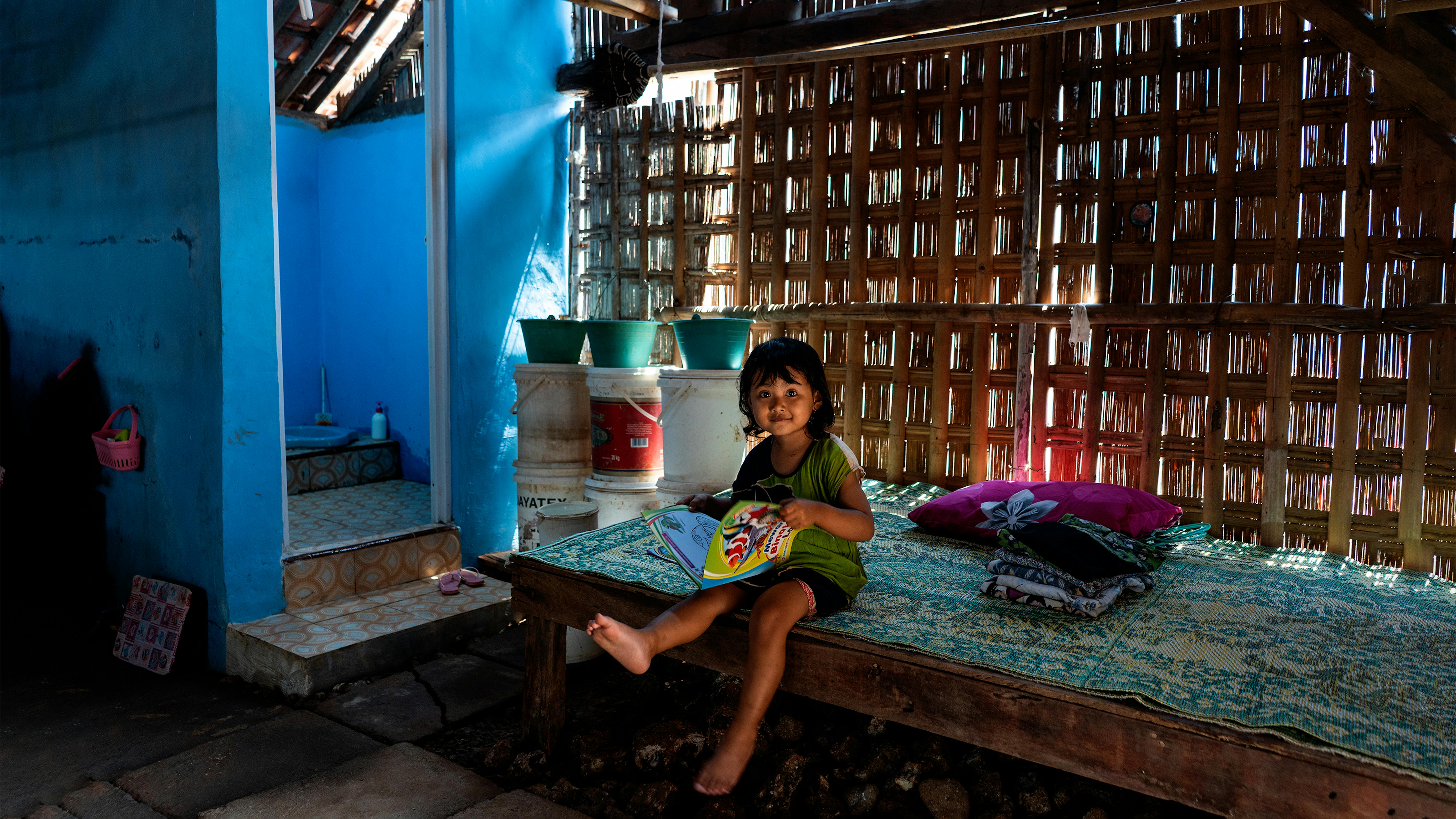 Indonesia, Fika, 3 anni, legge un libro vicino a un bagno di nuova costruzione nella sua casa nel villaggio di Tegaldowo