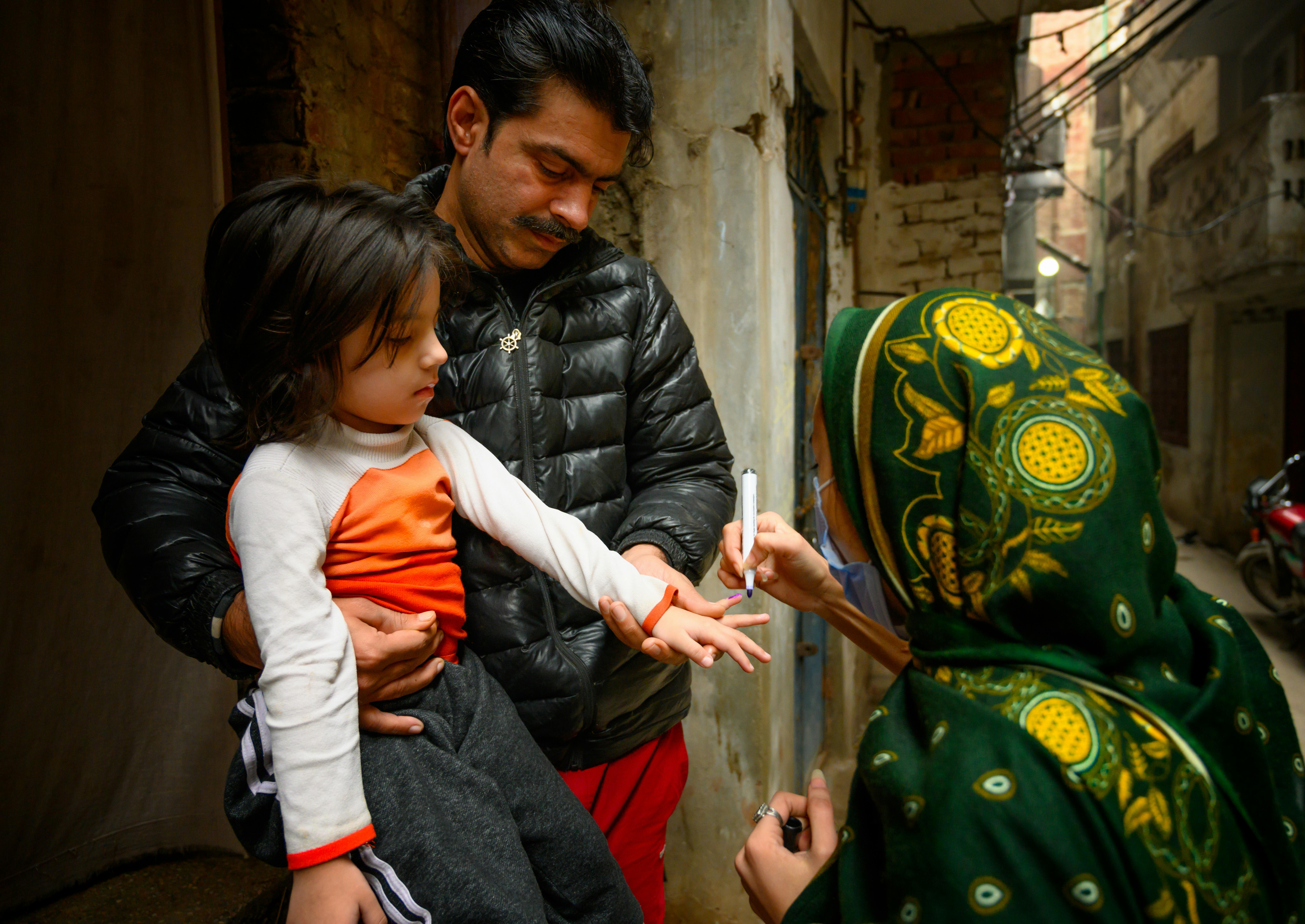 Pakistan, un'operatrice segna il dito della bambina in braccio al suo papà. La piccola è stata vaccinata contro la polio