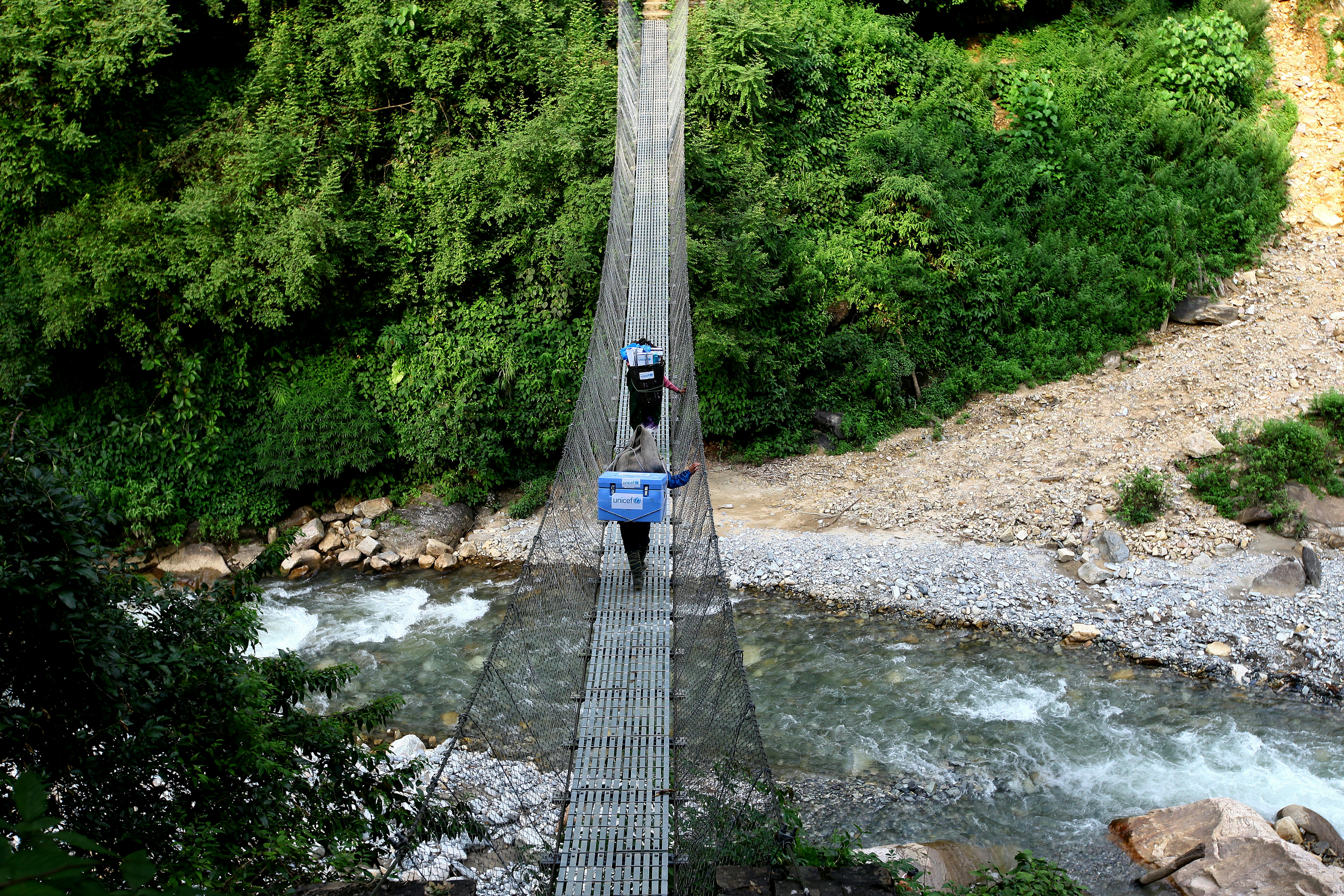 Nepal: un operatore sta trasportando i vaccini forniti dall'UNICEF attraverso un ponte sospeso su un fiume