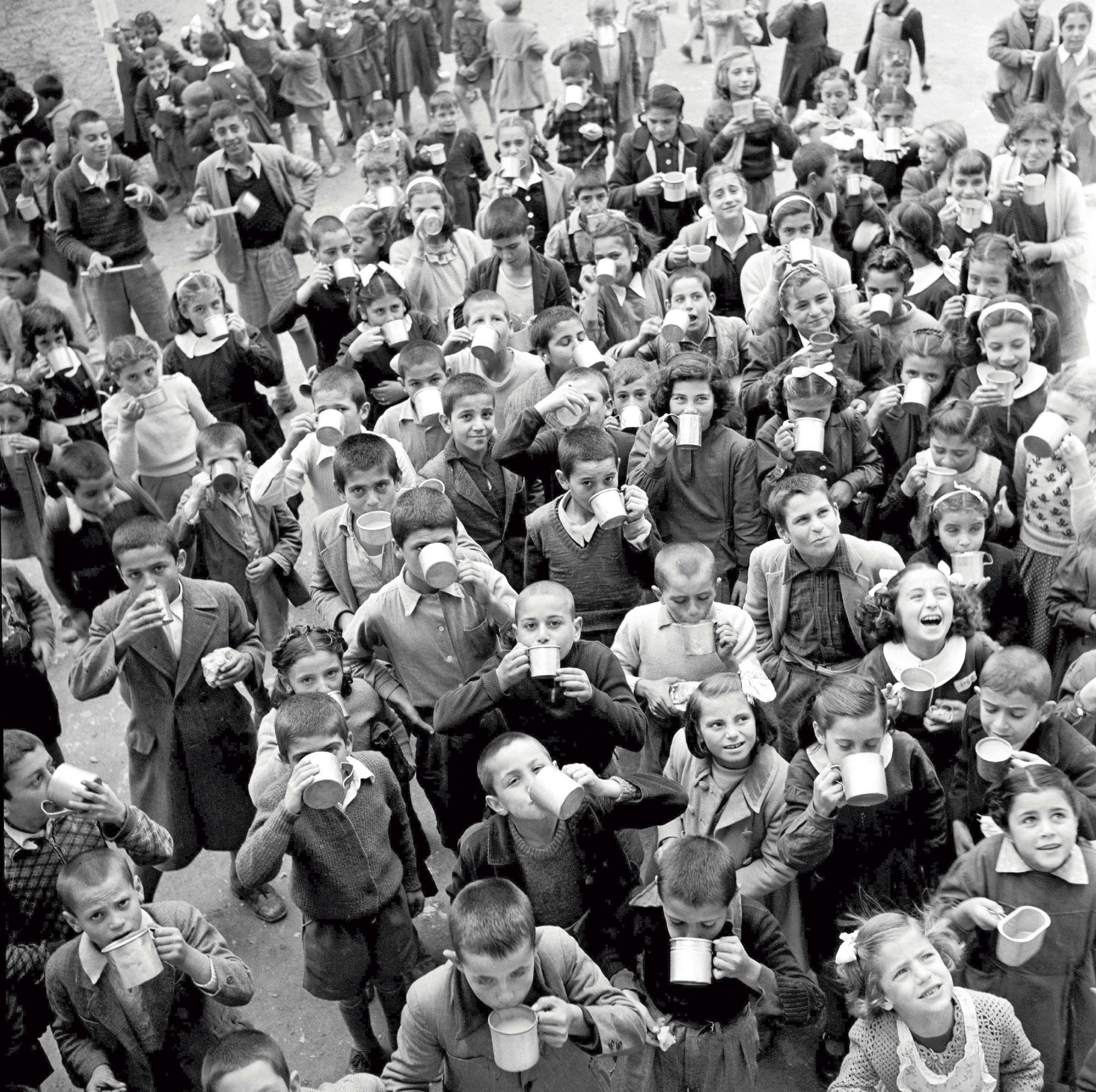 Grecia, 1951: bambini di una scuola elementare di Atene alzano le loro tazze di latta per bere il latte fornito dall'UNICEF