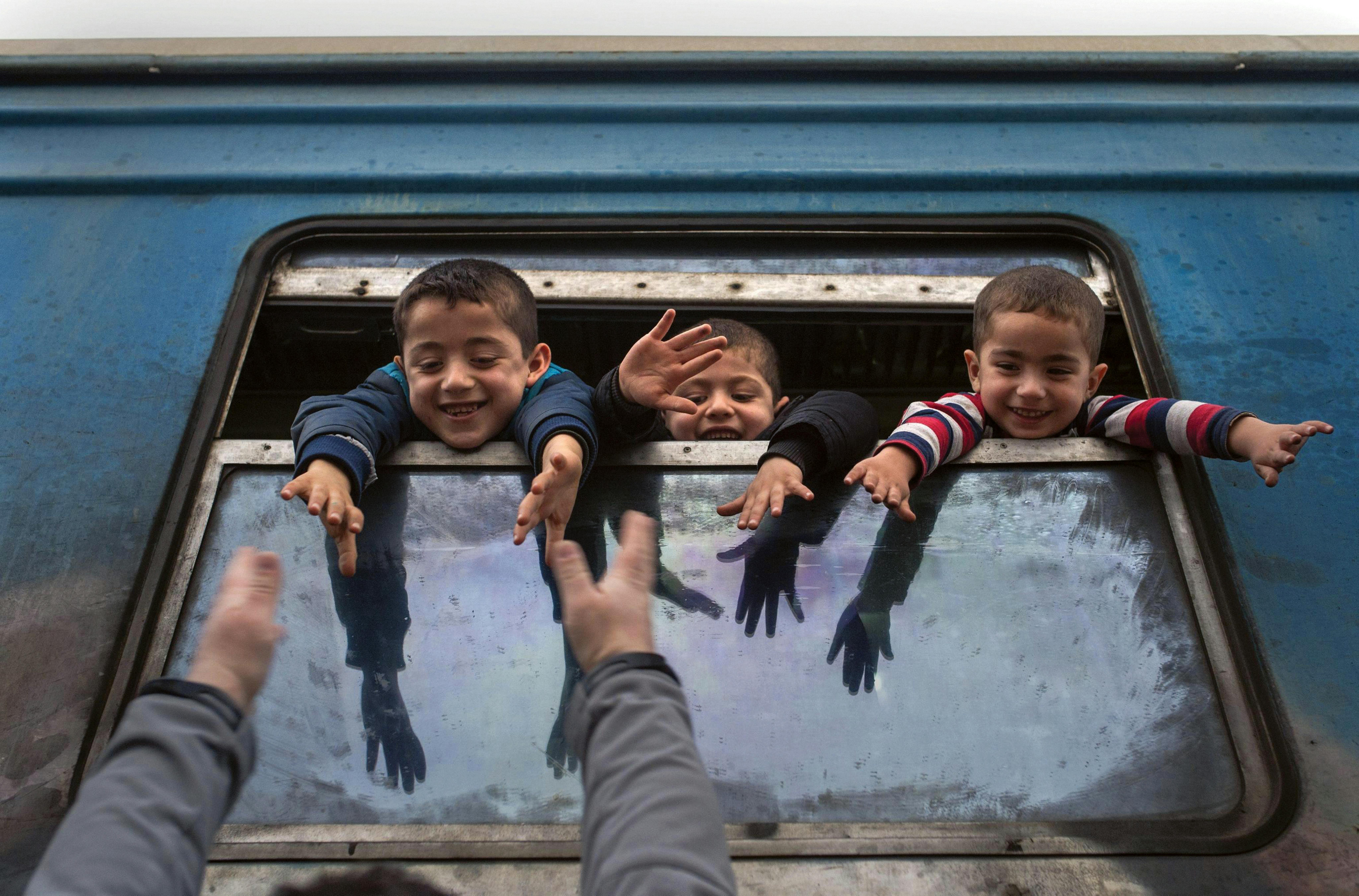 Macedonia, 2016. Bambini rifugiati salutano dai finestrini del treno diretto in Serbia. Migliaia di rifugiati continuano a passare attraverso la Macedonia nel loro cammino verso i paesi dell'Unione europea.