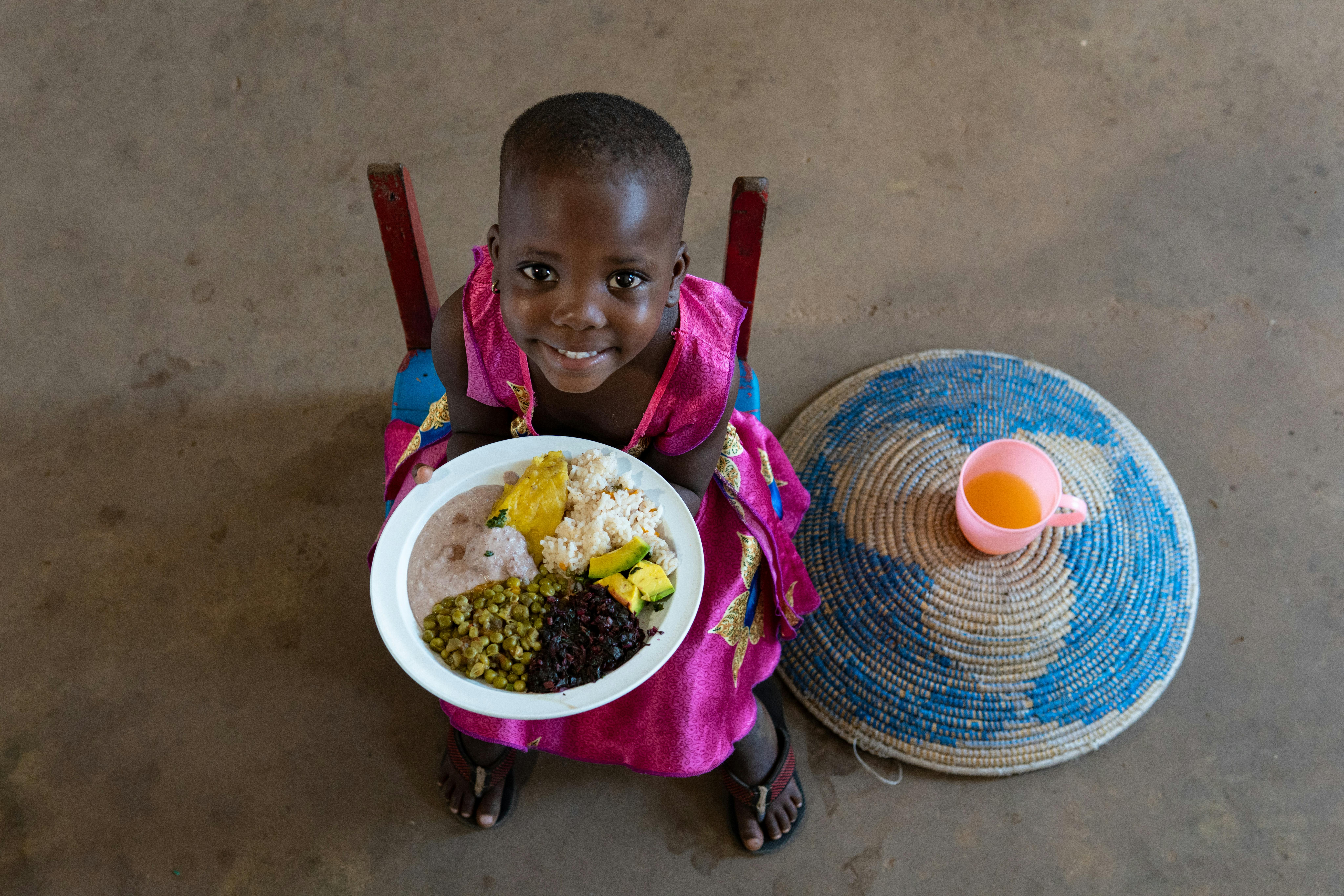 Uganda: Nakalema Betty, 3 anni, mostra la il suo pasto nutriente con riso, matooke (mash di banana), pasta di arachidi, verdure a foglia rossa, avocado e piselli.