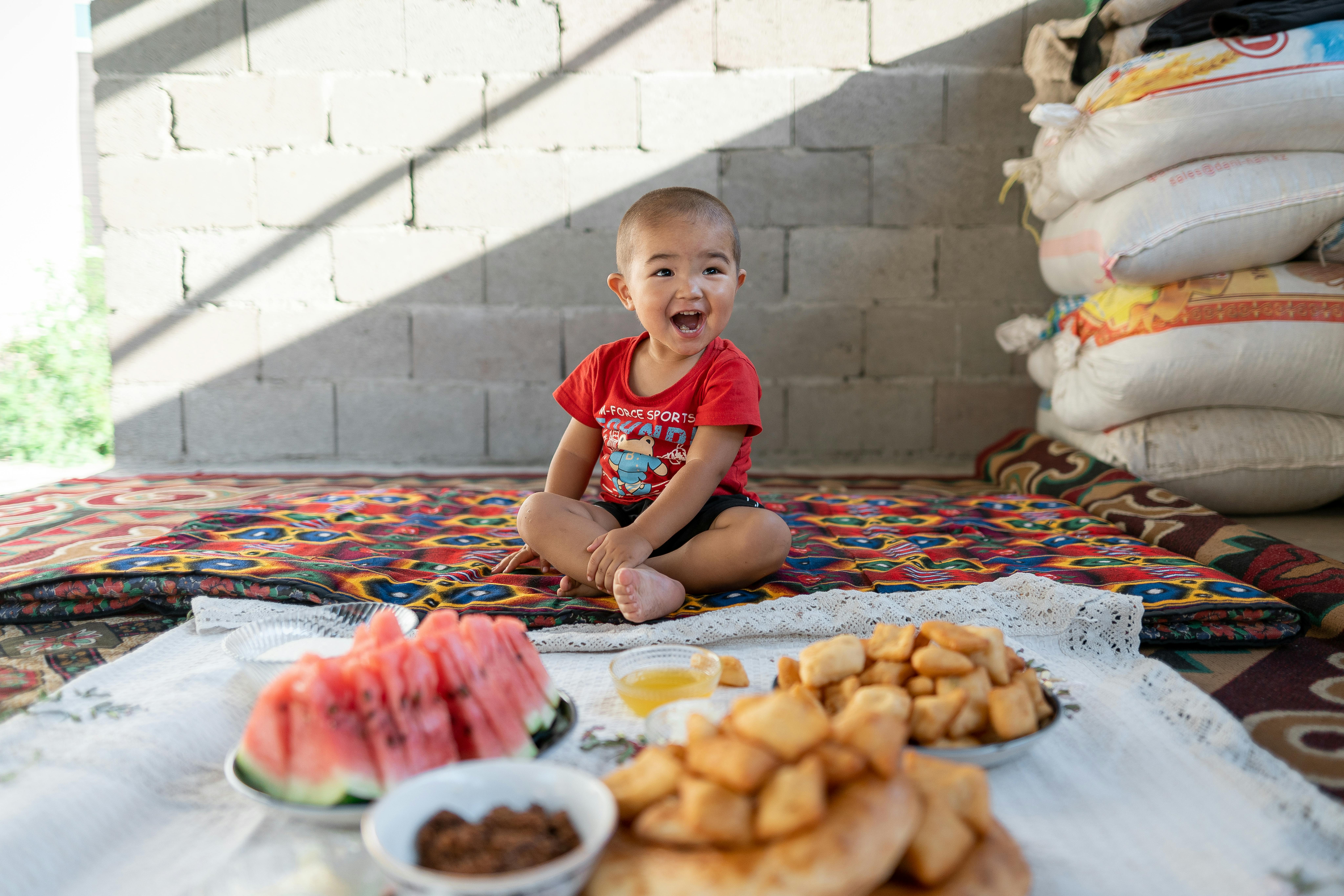 Ariet, 2 anni, siede sul pavimento accanto ad alcuni dei suoi cibi preferiti mentre si trova a casa, nel villaggio di Kurshab, in Kirghizistan