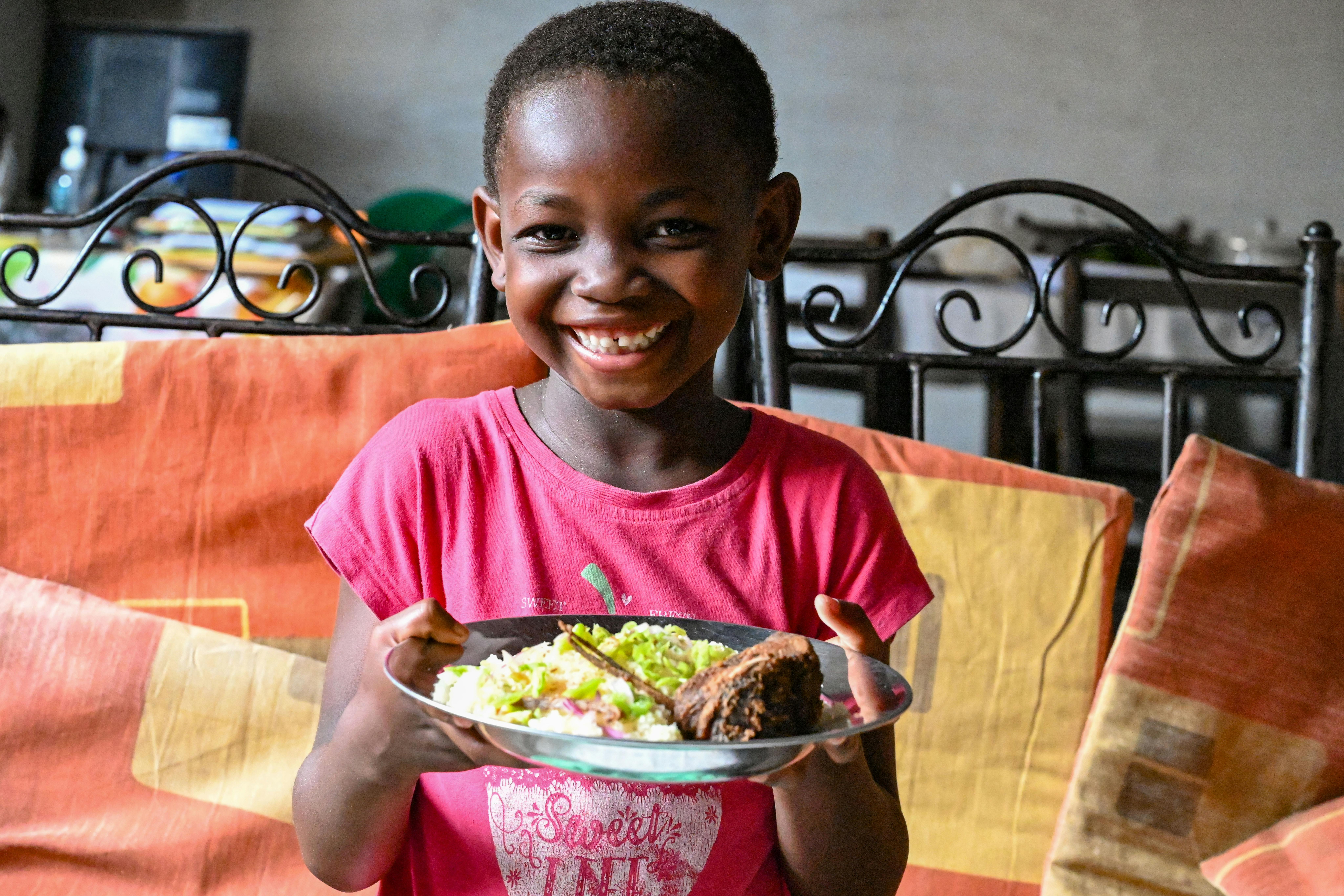 Auriane Esther, 6 anni, tiene in mano un piatto di Garba composto da una base di semolino di manioca, tonno fritto e verdure. Vive in Costa D'Avorio