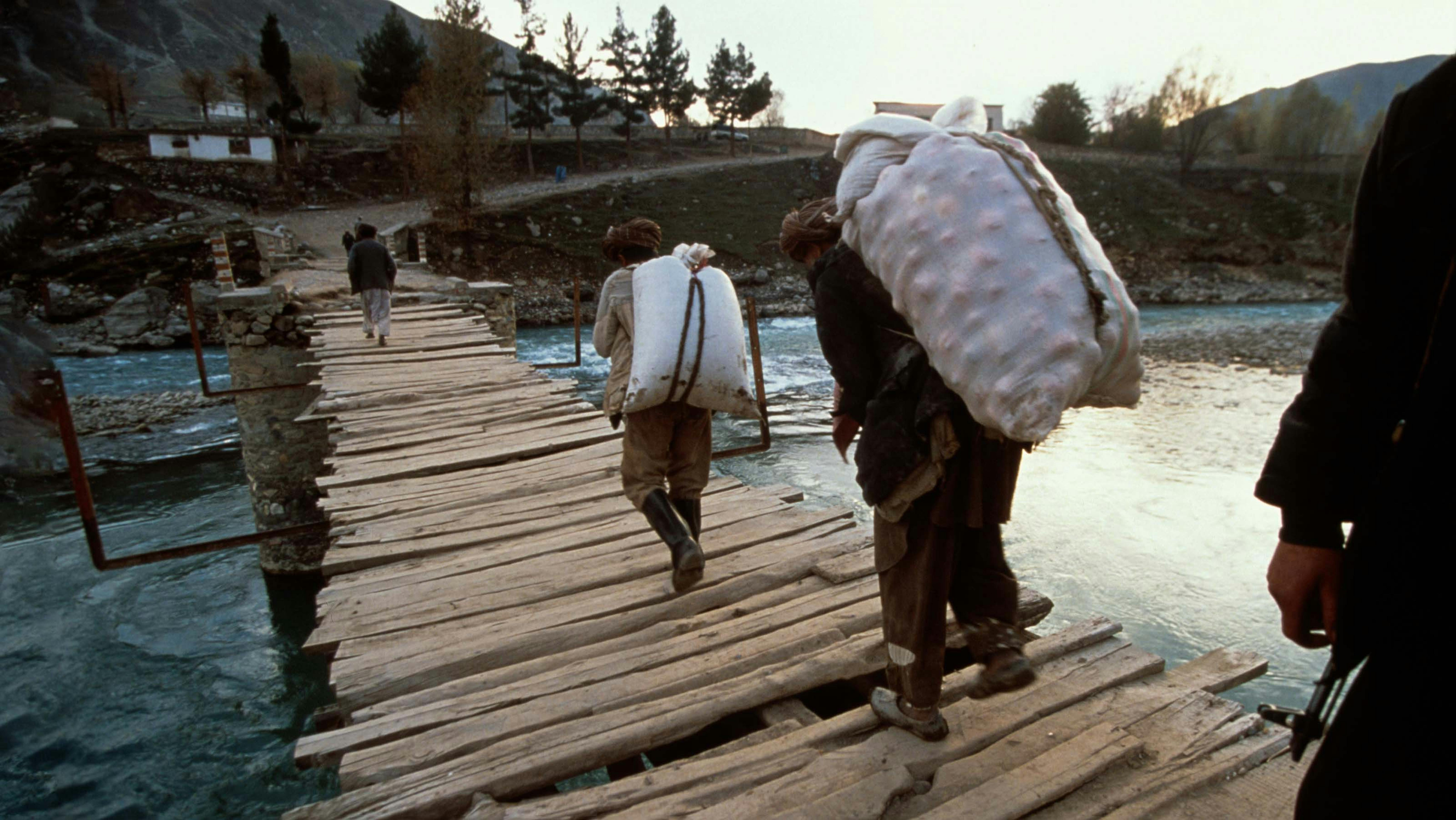 Un uomo armato osserva due uomini che trasportano dei sacchi. Siamo in Afghanistan nel 2000: durante il precedente governo dei talebani