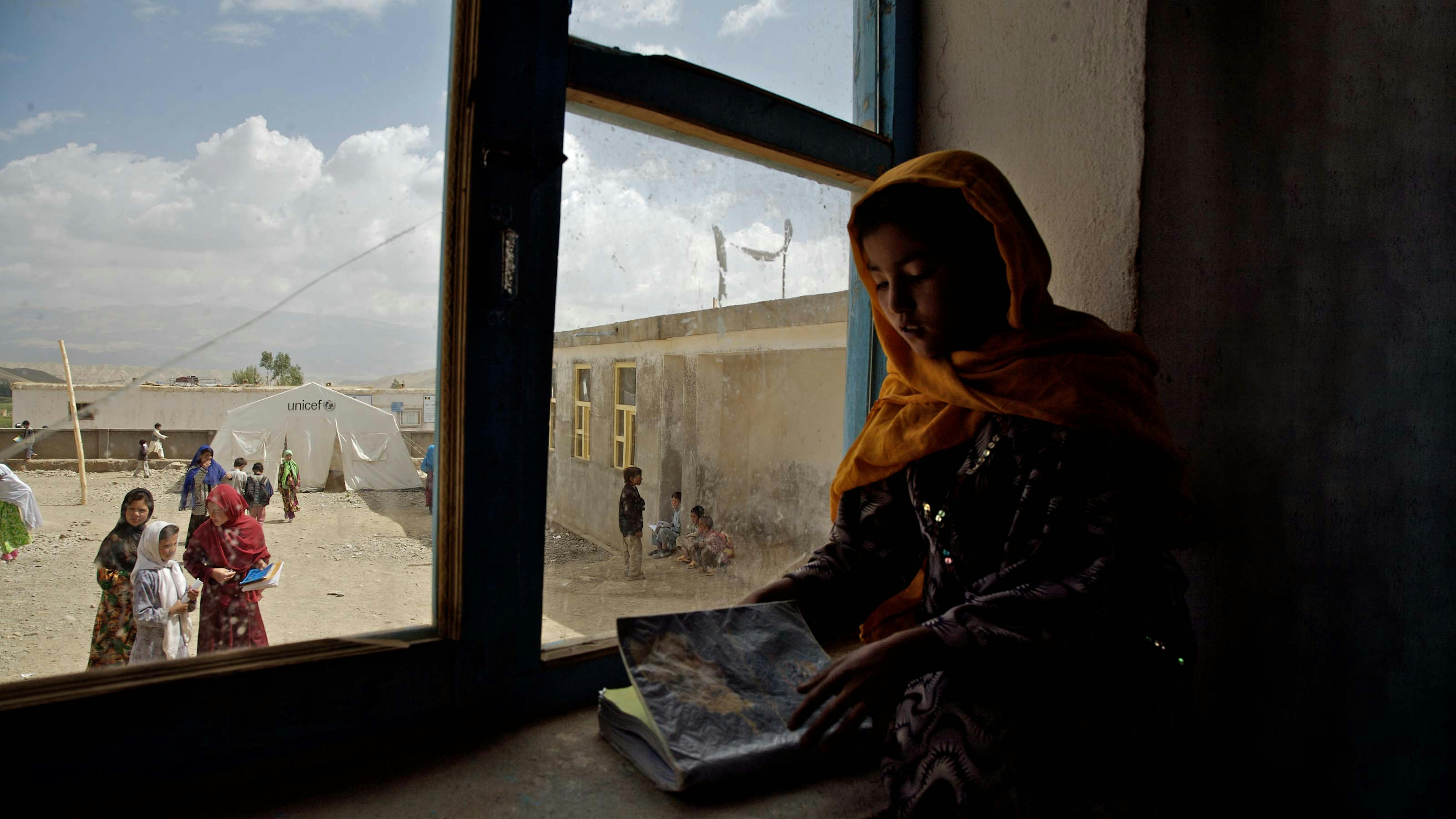 Una bambina apre un libro davanti a una finestra a Bam Sarai, Afghanistan