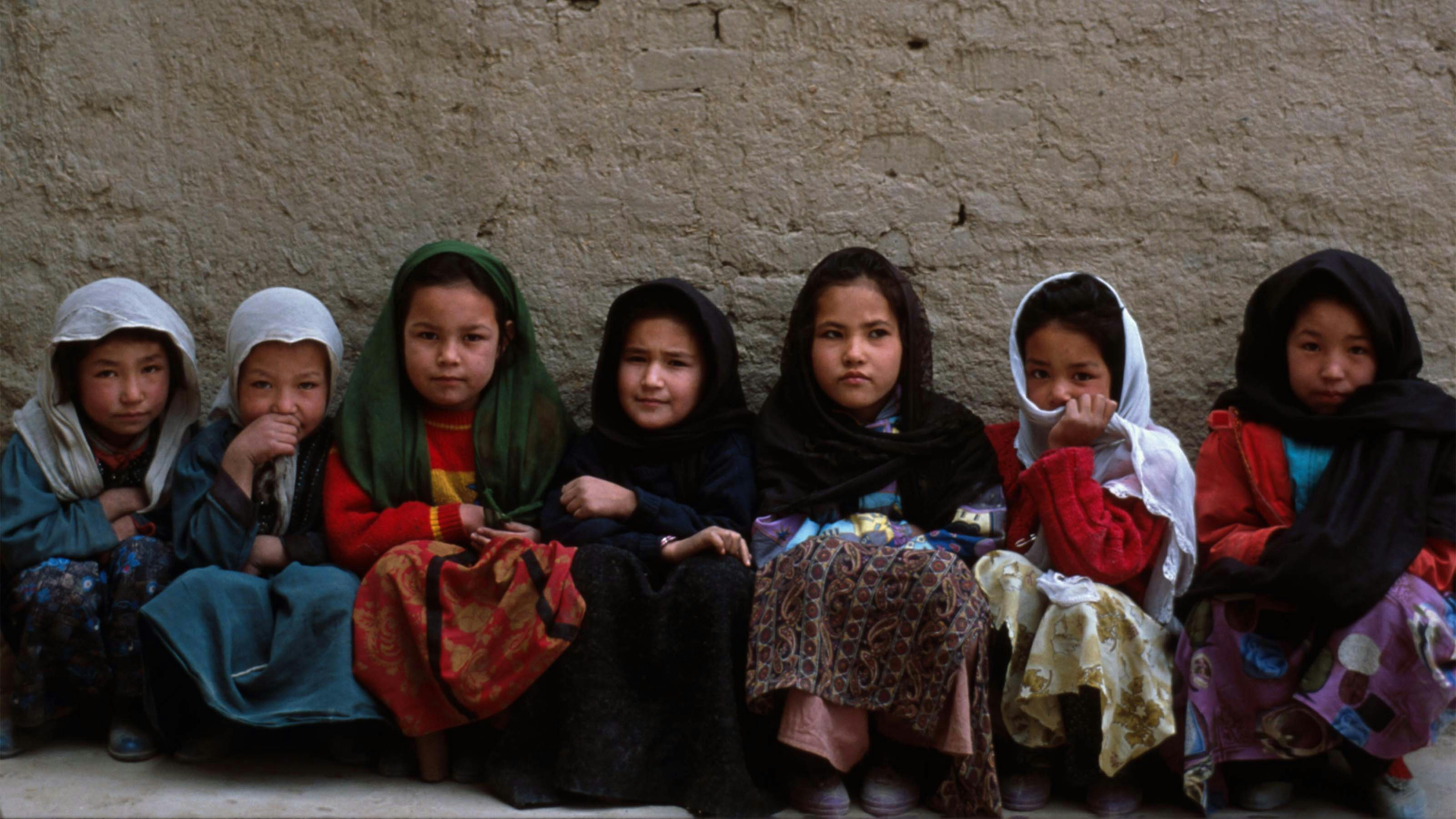 Bambine afghane sedute in fila addosso a un muro della scuola di Dasht-e-Barchi a Kabul, siamo nel 2008