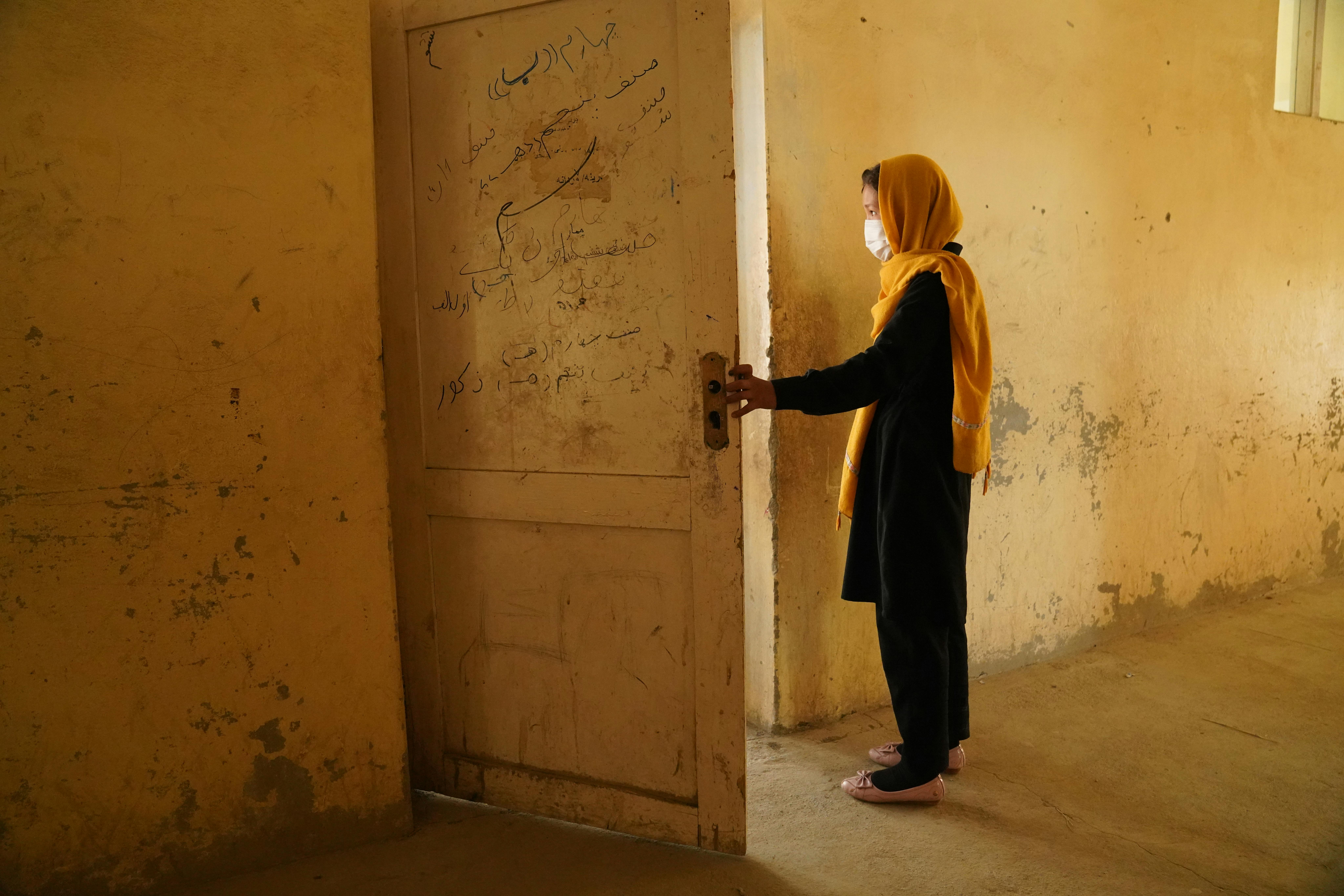 Una ragazza afghana apre la porta e guarda fuori. L'8 maggio 2021, un attacco contro gli studenti che terminavano le lezioni ha distrutto la scuola di Sayed ul-Shuhada ha ucciso 85 persone, 42 delle quali ragazze, e ne ha ferite più di 200.