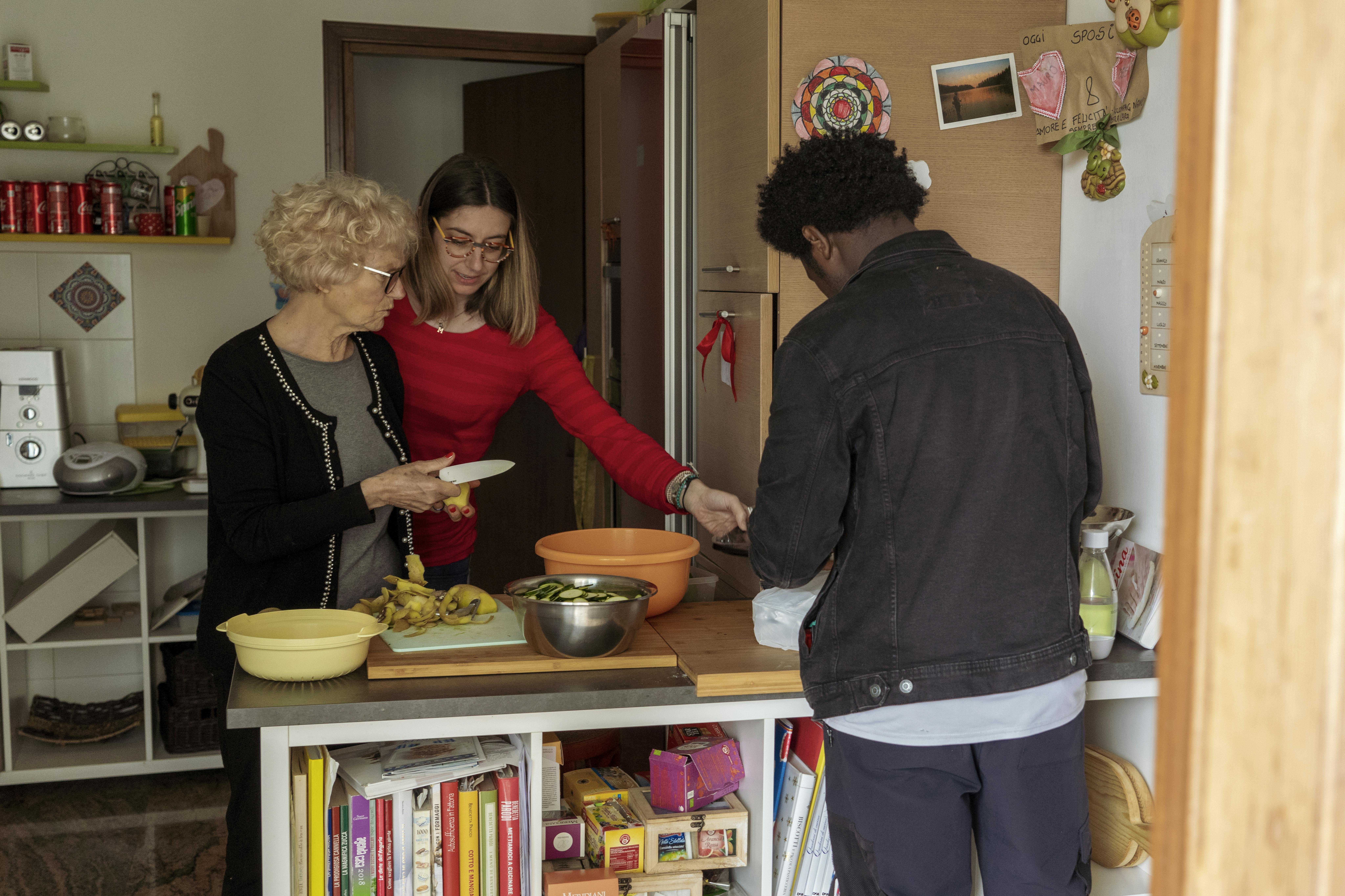 La famiglia prepara il pranzo in cucina. Desjrè, madre affidataria di Mamajang, parla del programma di affido , "Credo che la sfida più grande sia trovare un posto per i minori non accompagnati in tutti i sensi: trovare un posto dove possano stare fisicamente ma anche dove si sentano amati." 