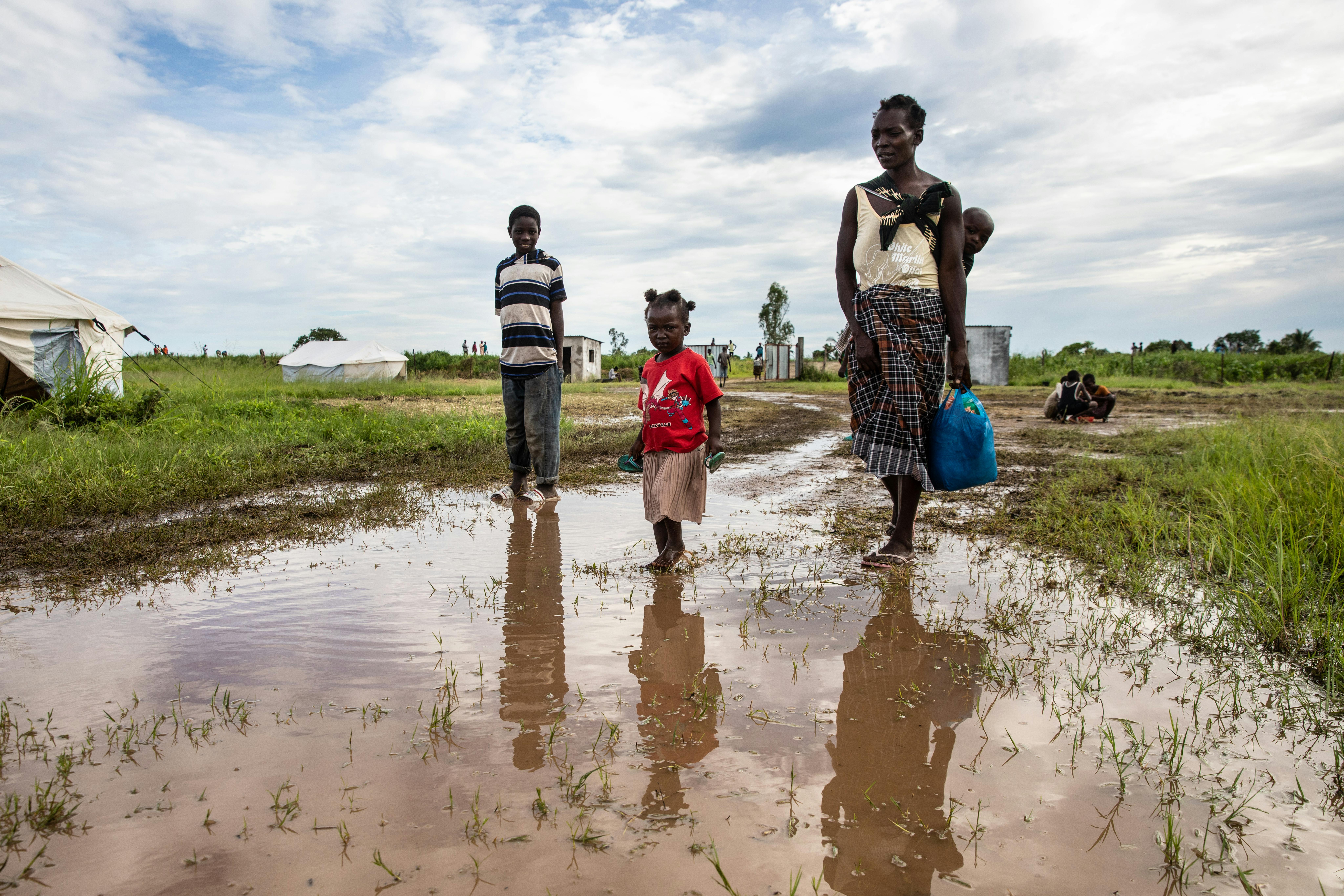 Una donna con il suo bambino sulle spalle e altri bambini al seguito, si dirige verso un centro di trasferimento passando per un'area allagata in Mozambico. 