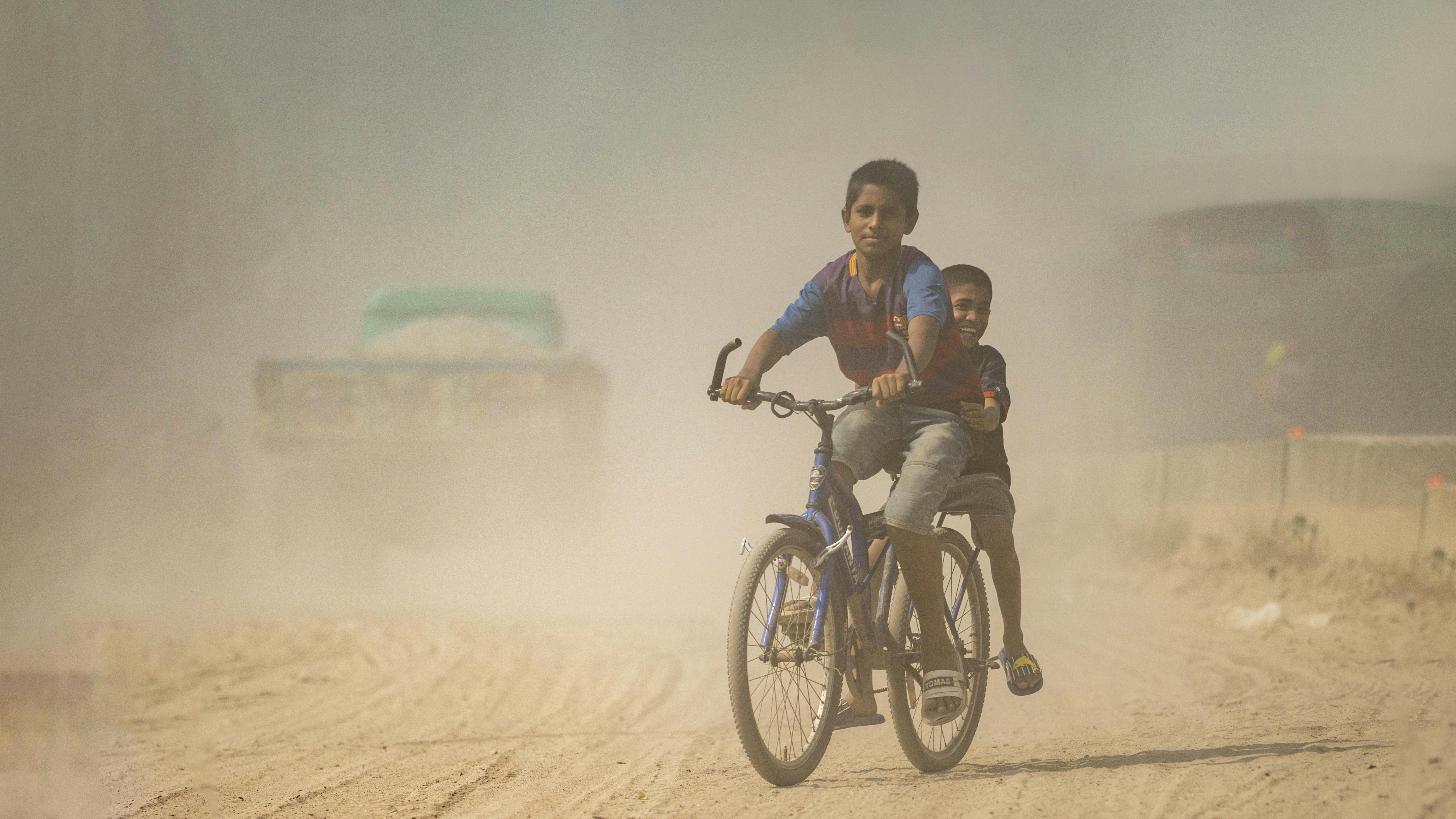 Bambini in bicicletta su una strada polverosa a Dacca, in Bangladesh