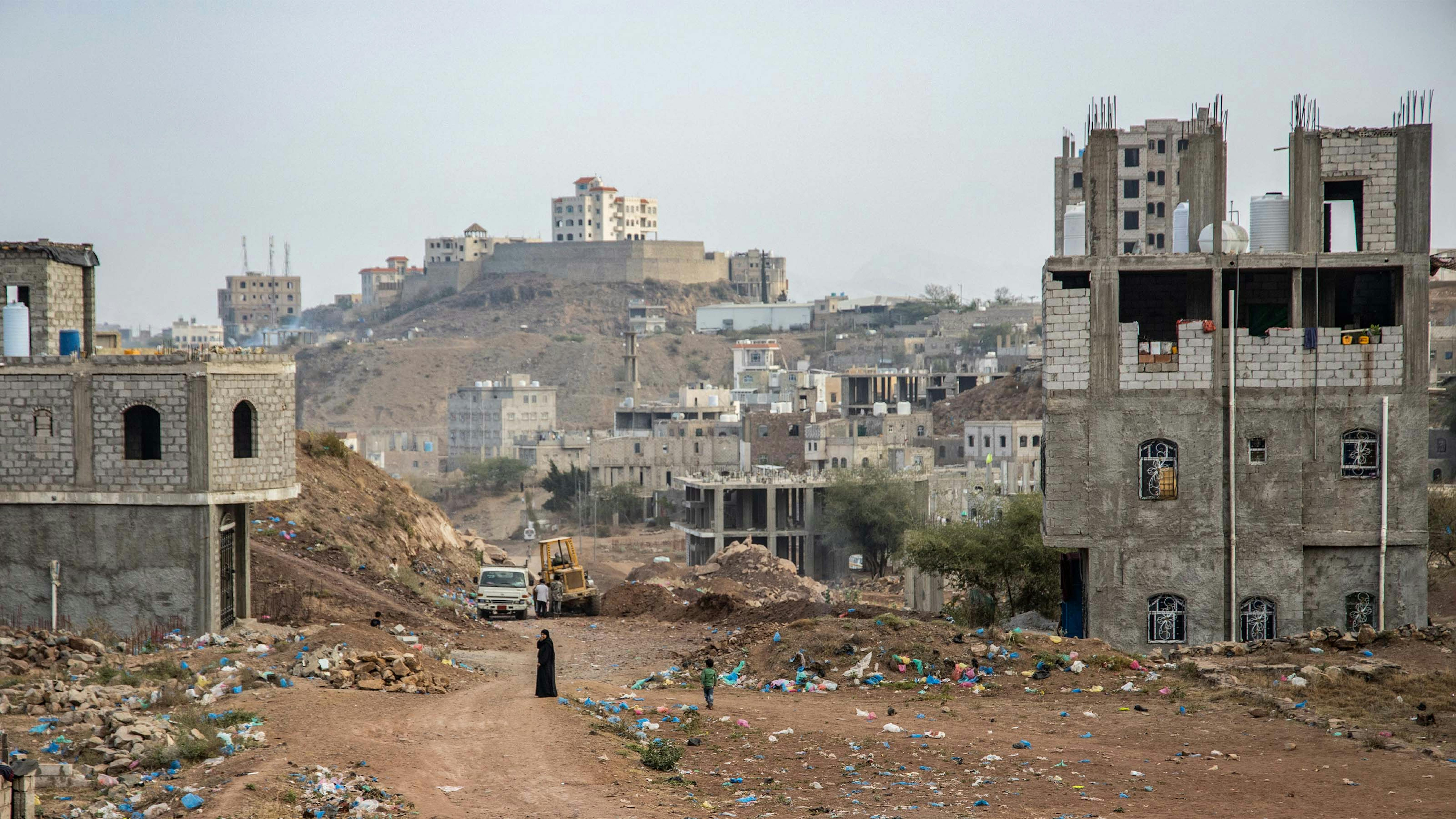 Yemen: una donna cammina tra le macerie e i rifiuti della città di Taizz, completamente distrutta
