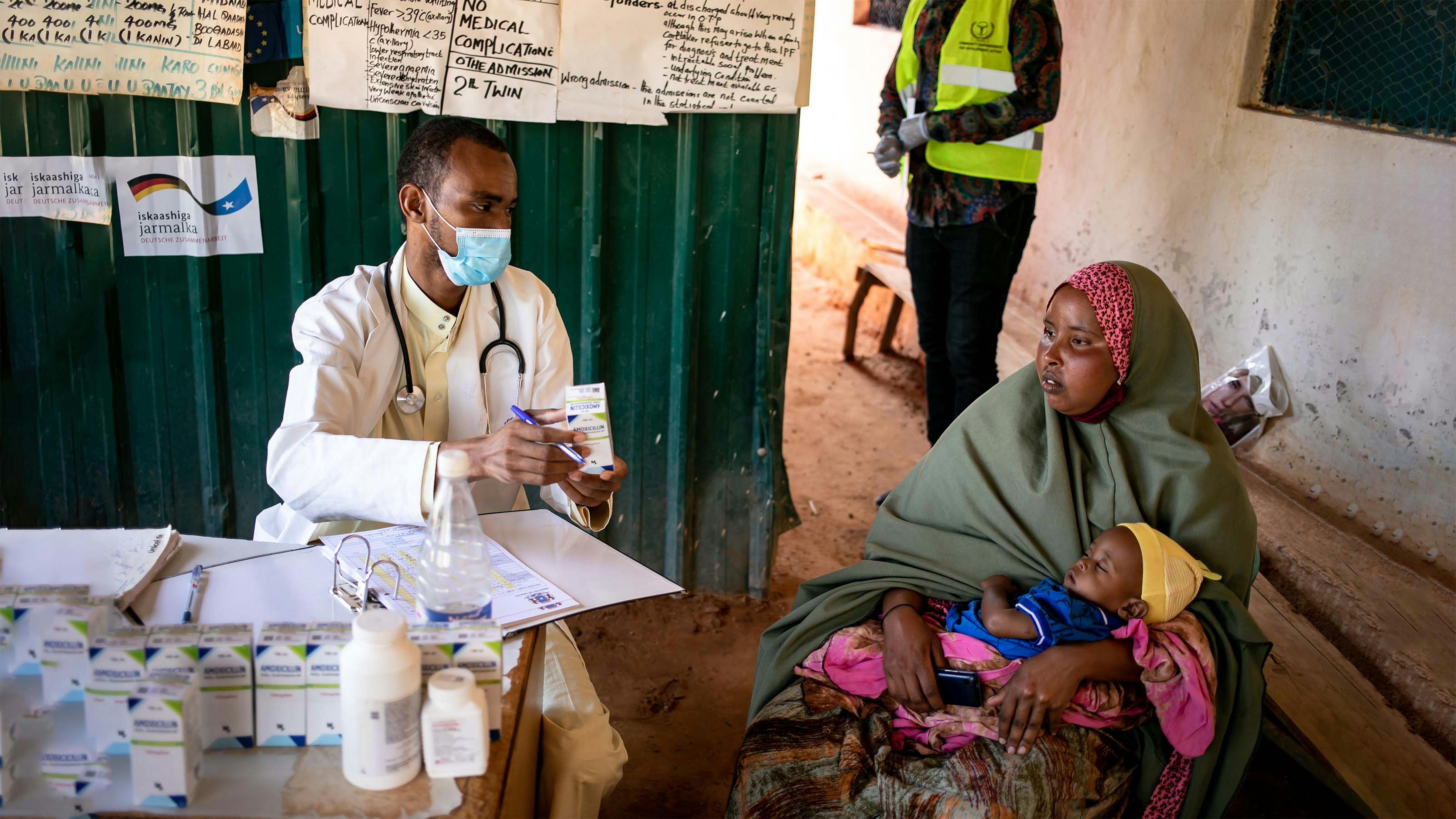 Somalia, Il dottor Abdirahman Abdishakur, 31 anni, consegna dei farmaci  una donna con bambino al Dolow Health Center di Dolow