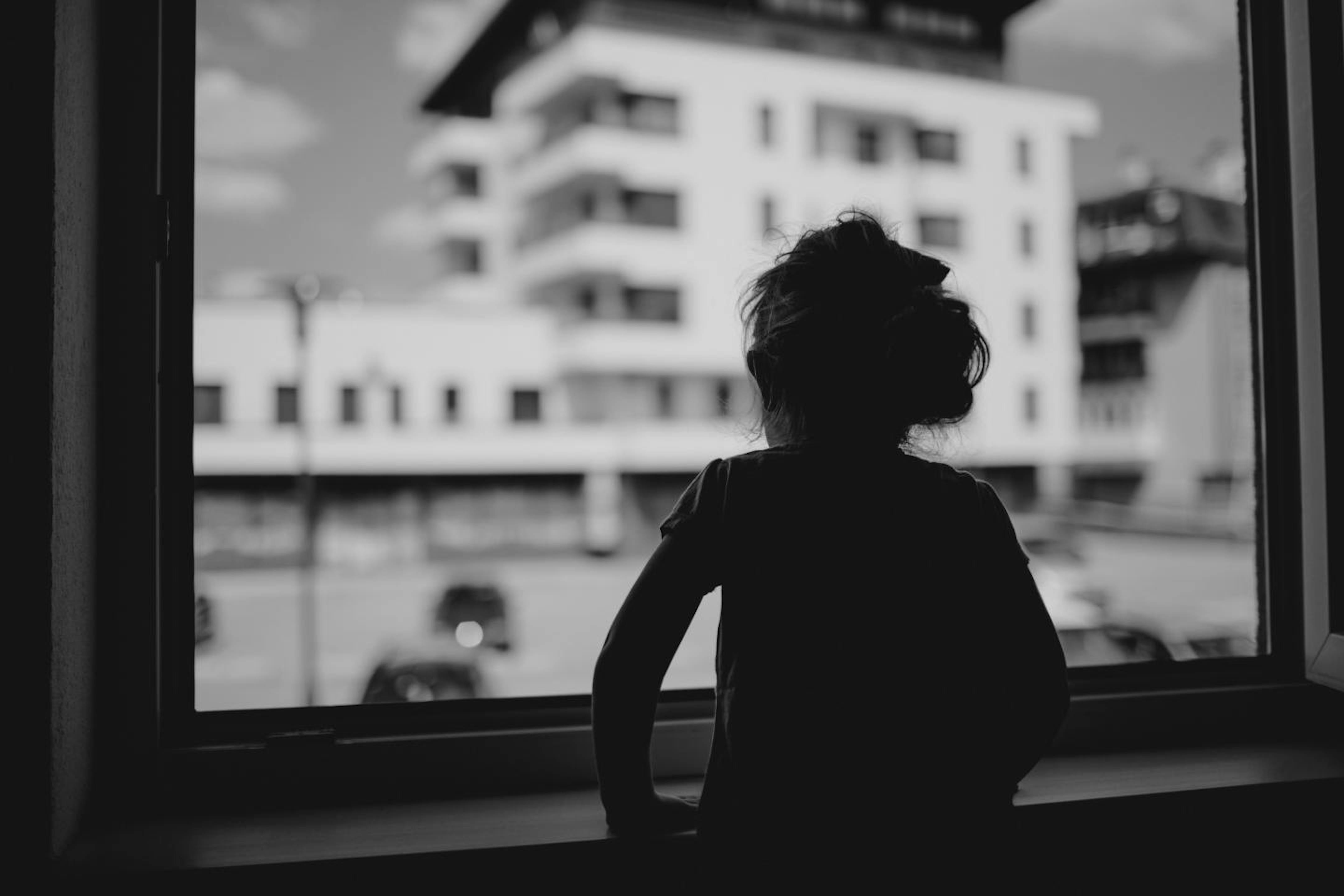 Bambina di spalle guarda fuori dalla finestra