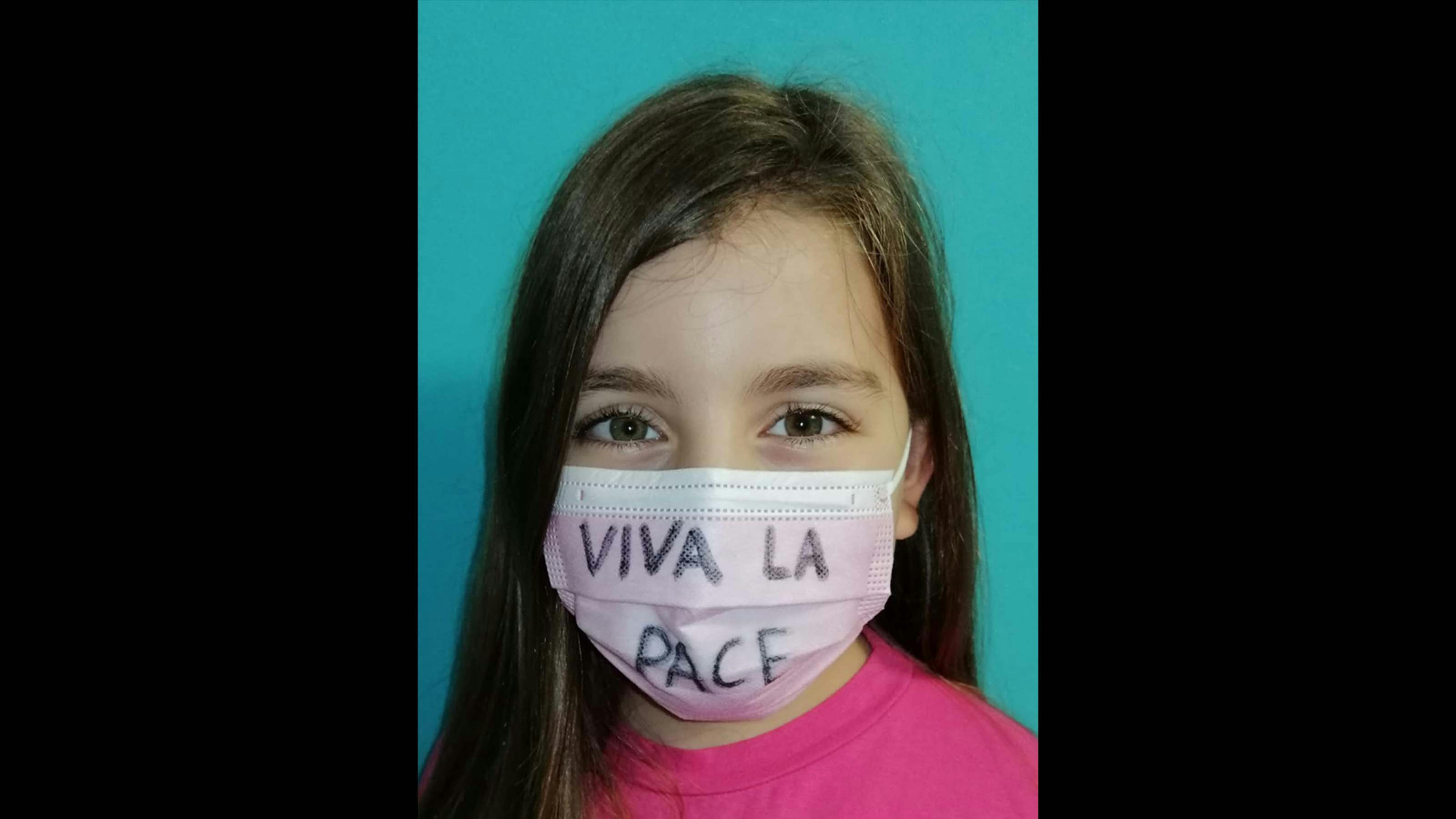 Una bambina indossa una mascherina con un messaggio di pace