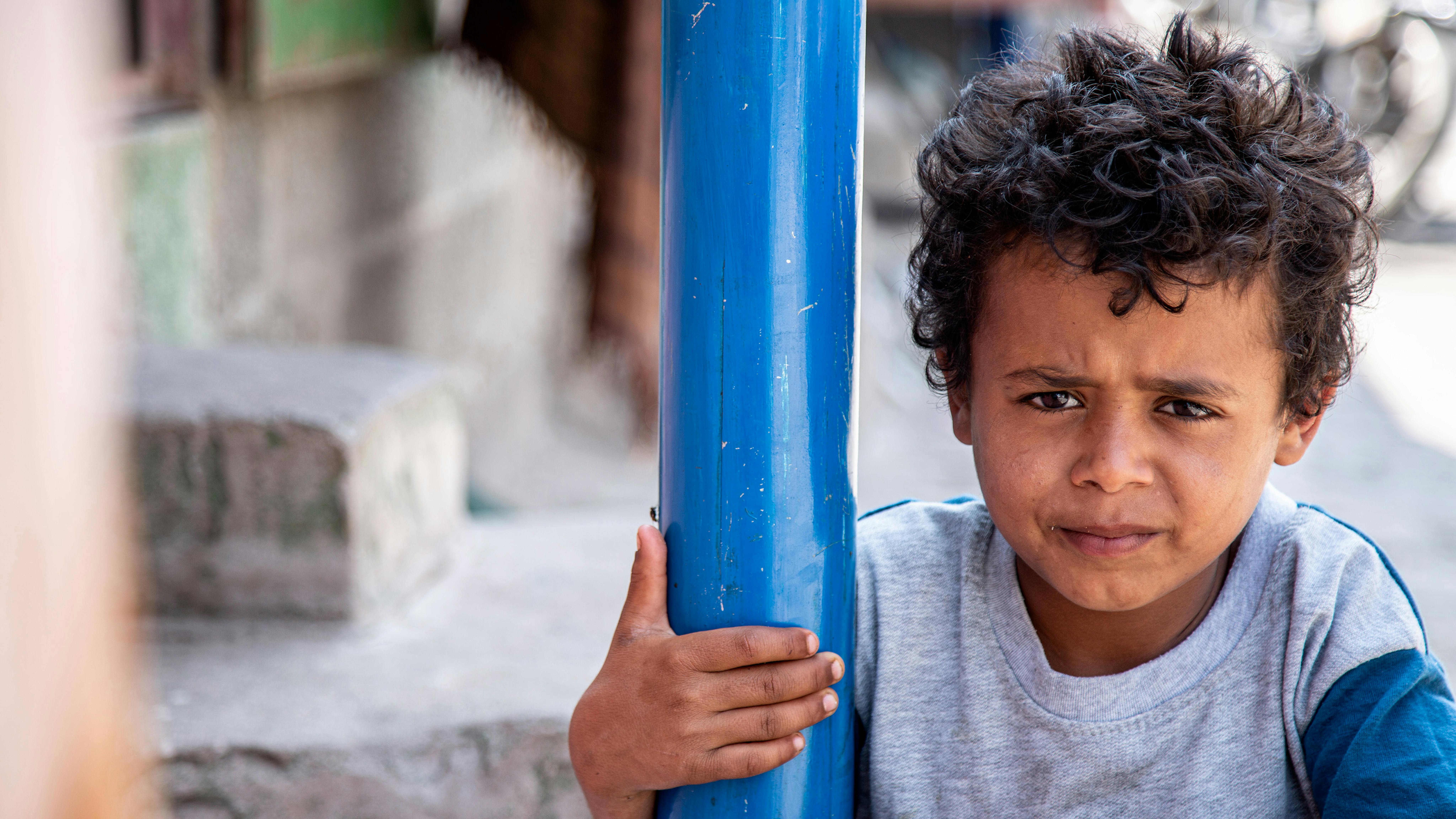 Yemen, Un bambino resta in disparte mentre gli altri giocano con l'acqua dopo aver sofferto per la scarsità d'acqua nel campo per sfollati interni di Ibb