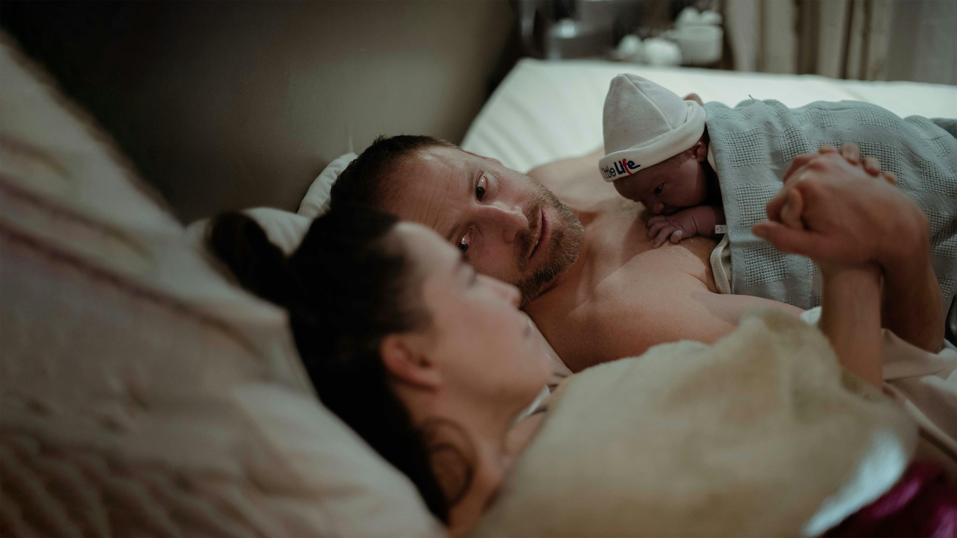 mamma e papà con neonato nel letto