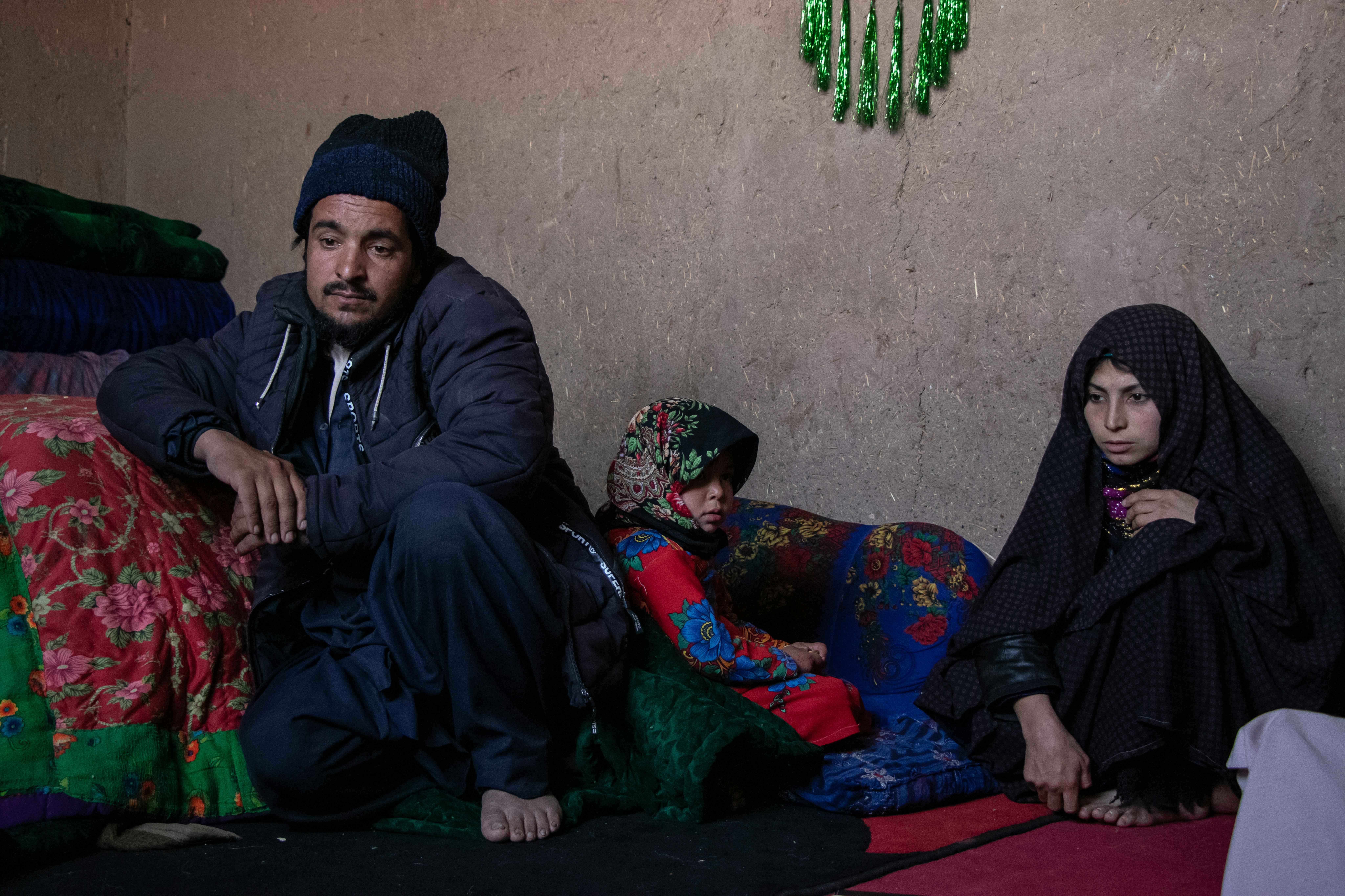Farhana, 5 anni, è accovacciata tra suo padre Karim e sua madre Nasrin. L'intera famiglia, composta da 5 persone, vive nella casa di una stanza, fatta di pareti di fango, all'interno del campo per sfollati interni ad Herat, Afghanistan. Sono molto poveri, sono dovuti scappare dalla loro casa per i debiti contratti.