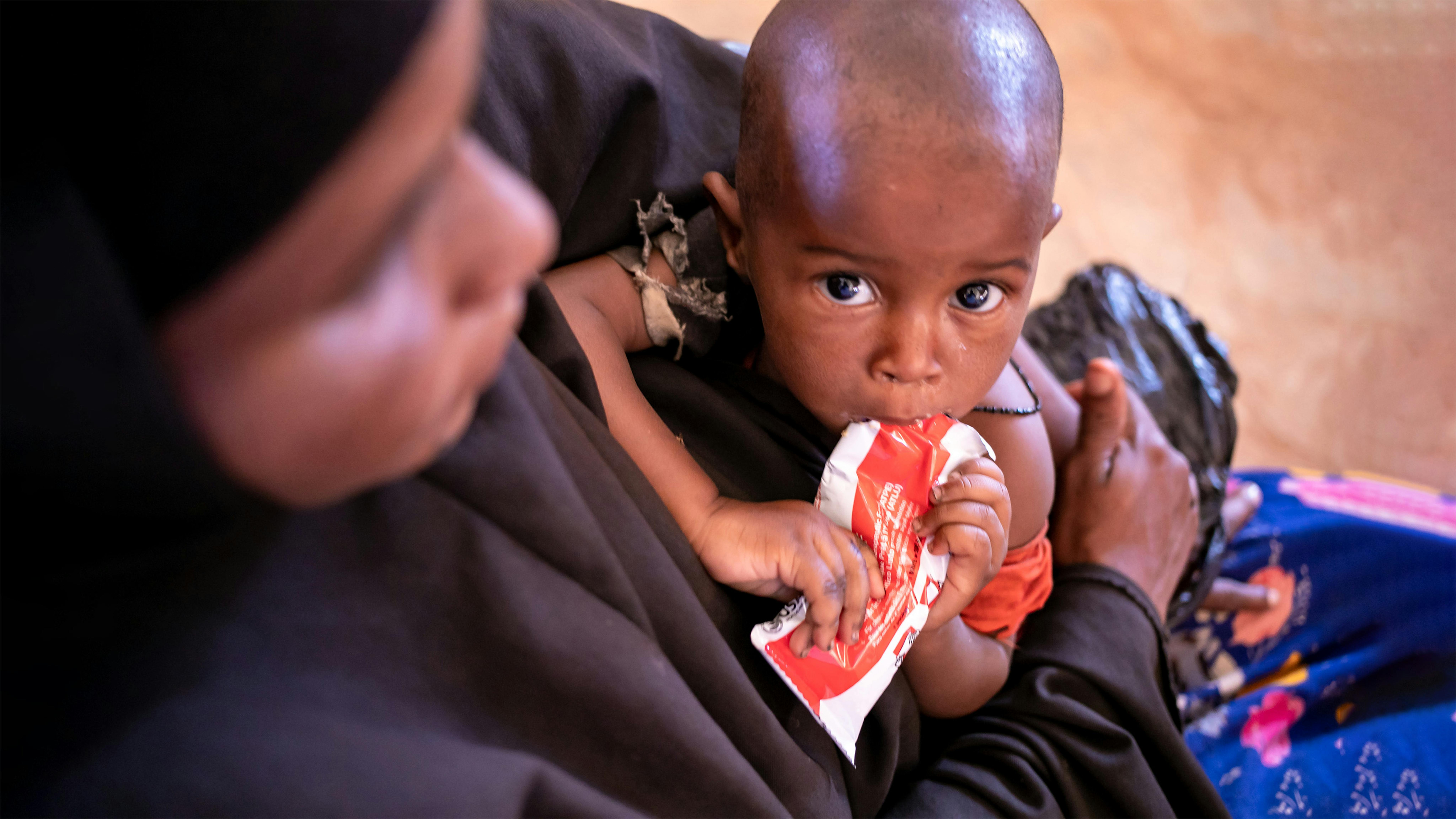 Un bambino è tenuto in braccio da sua madre mentre si nutre di una bustina di cibo terapeutico pronto all'uso in Somalia.