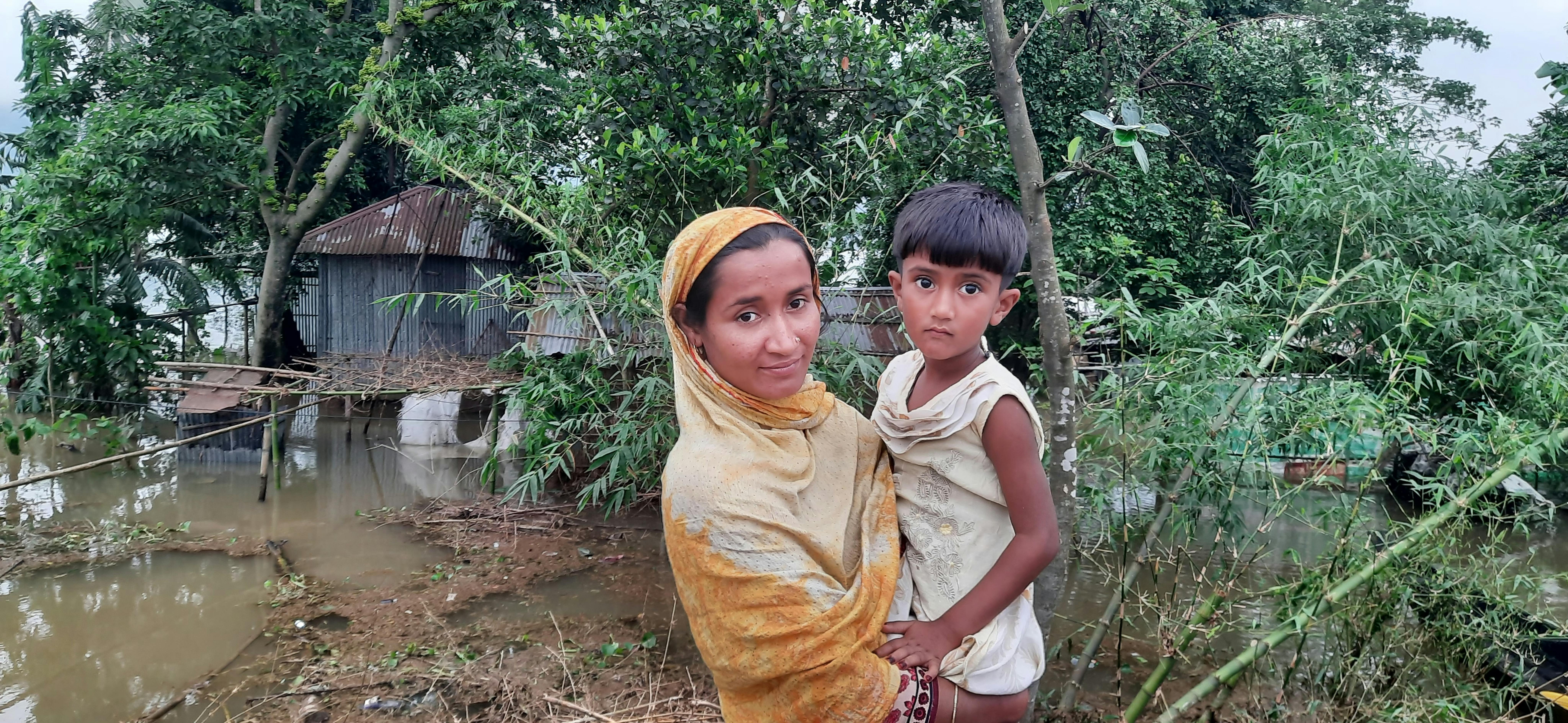 Una madre e un bambino  fuori dalla loro casa di lamiera, inondata dall'alluvione a Jaintapur, Sylhet