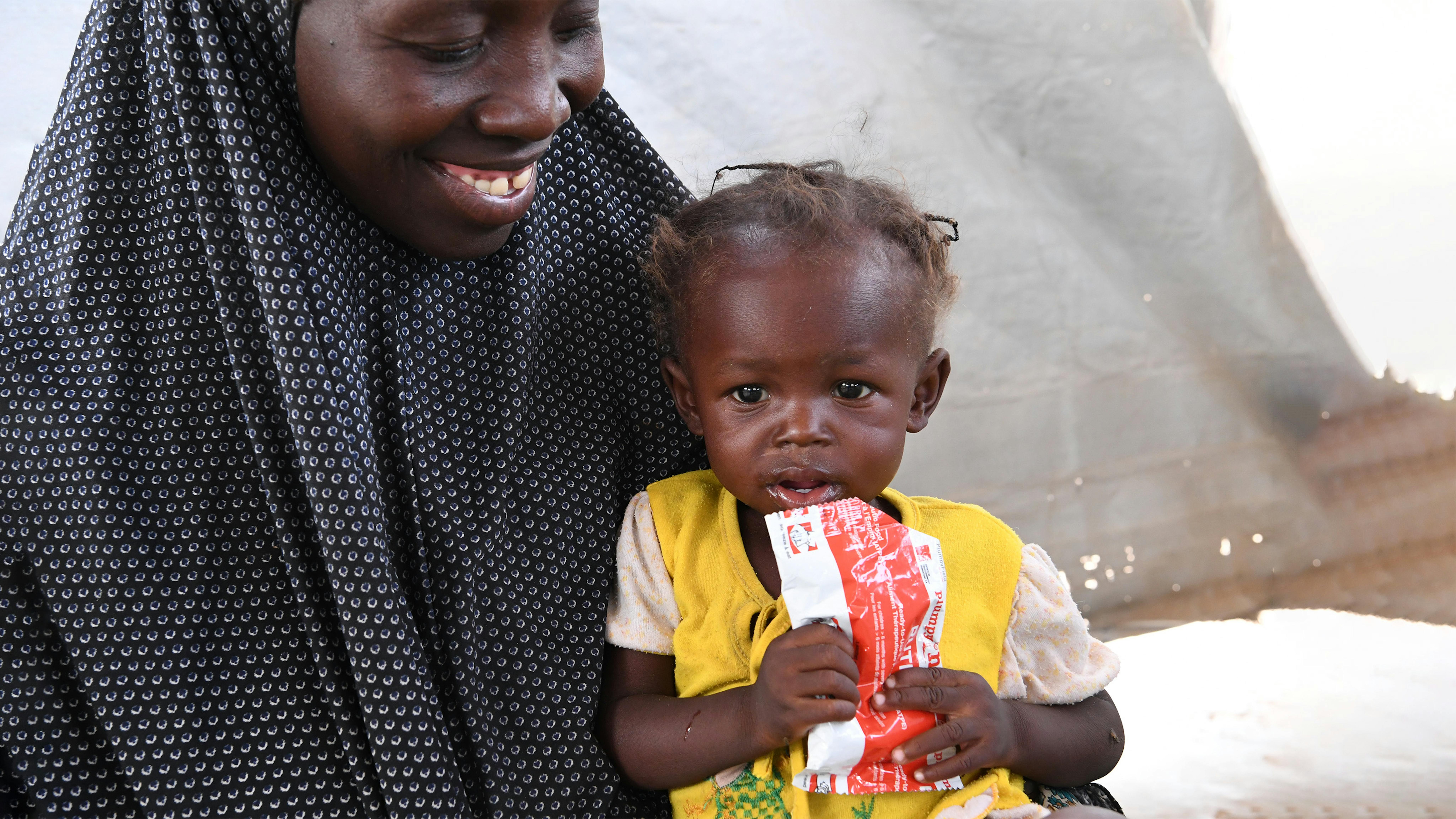 Niger, Biba, 35 anni, tiene in braccio la figlia di 2 anni Anifa mentre mangia un pacchetto di alimenti terapeutici pronti per l'uso (RUTF)