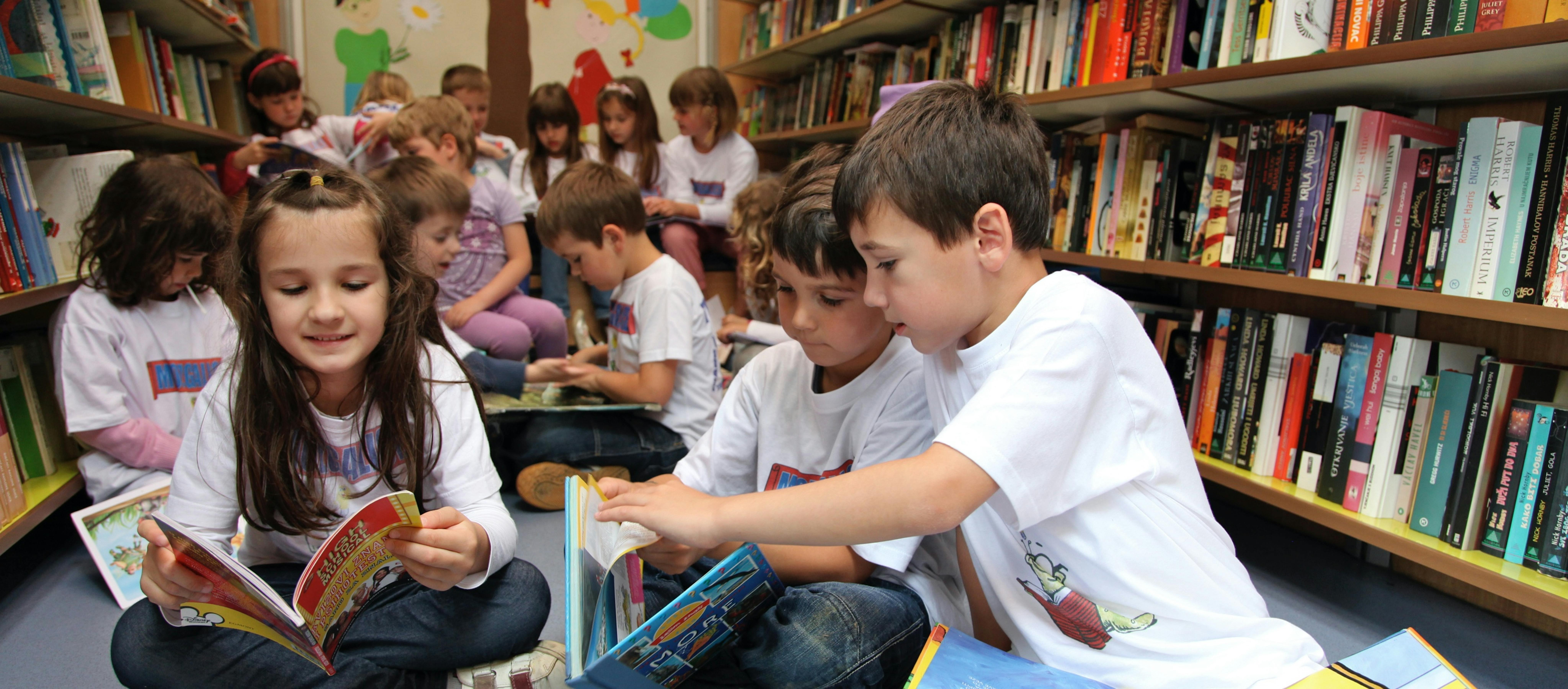 Bambini leggono seduti a terra in una biblioteca