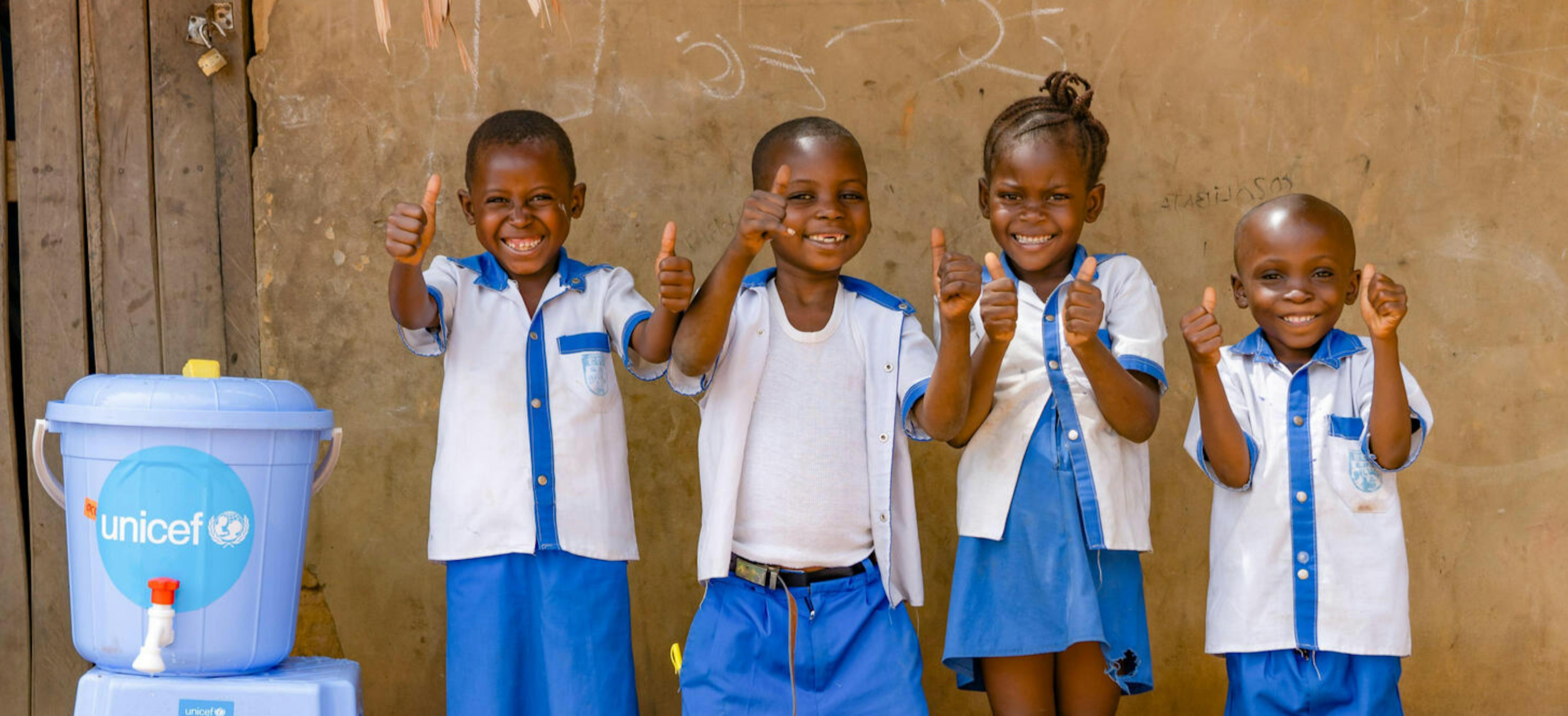 Bambini della scuola primaria Ilako a Mbandaka, Rep. Democratica del Congo, sorridono vicino alle forniture di acqua installate da UNICEF nelle scuole