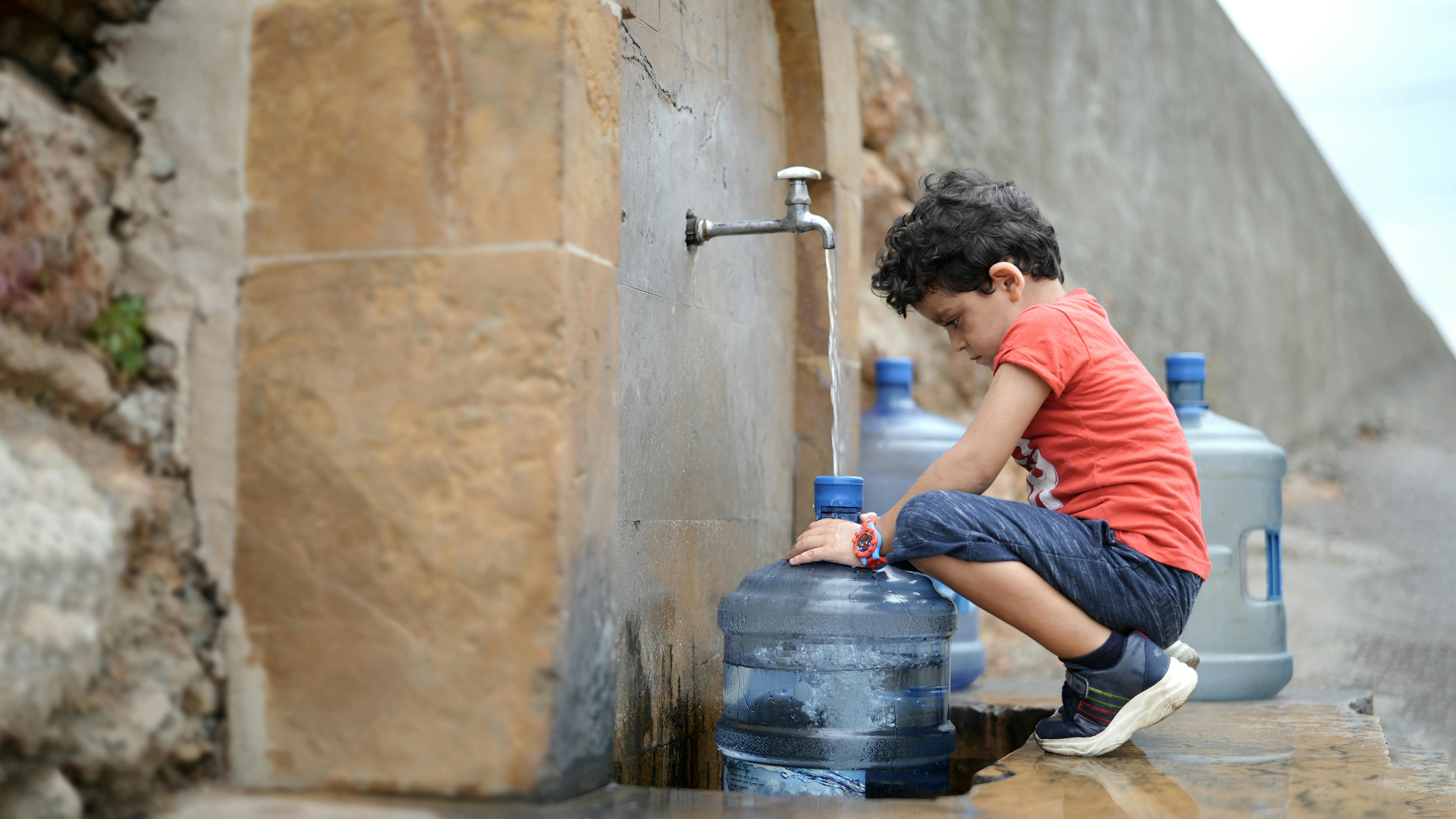 Libano - Georgio, 4 anni, sta aiutando i suoi genitori a riempire i loro piccoli contenitori perché non hanno acqua in casa.