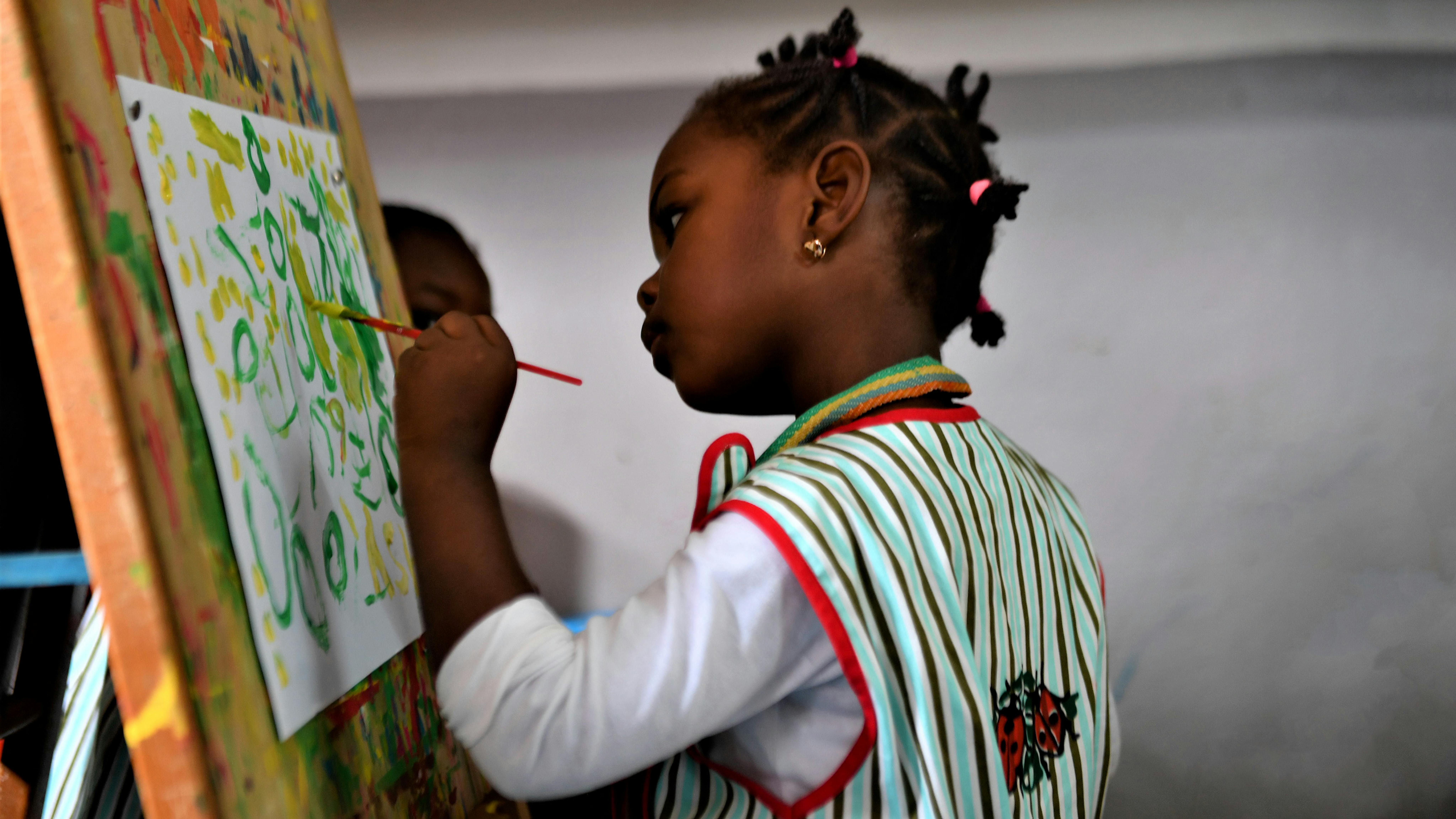 Camerun, una ragazza dipinge su una tela posta su un banco da disegno durante una lezione scolastica