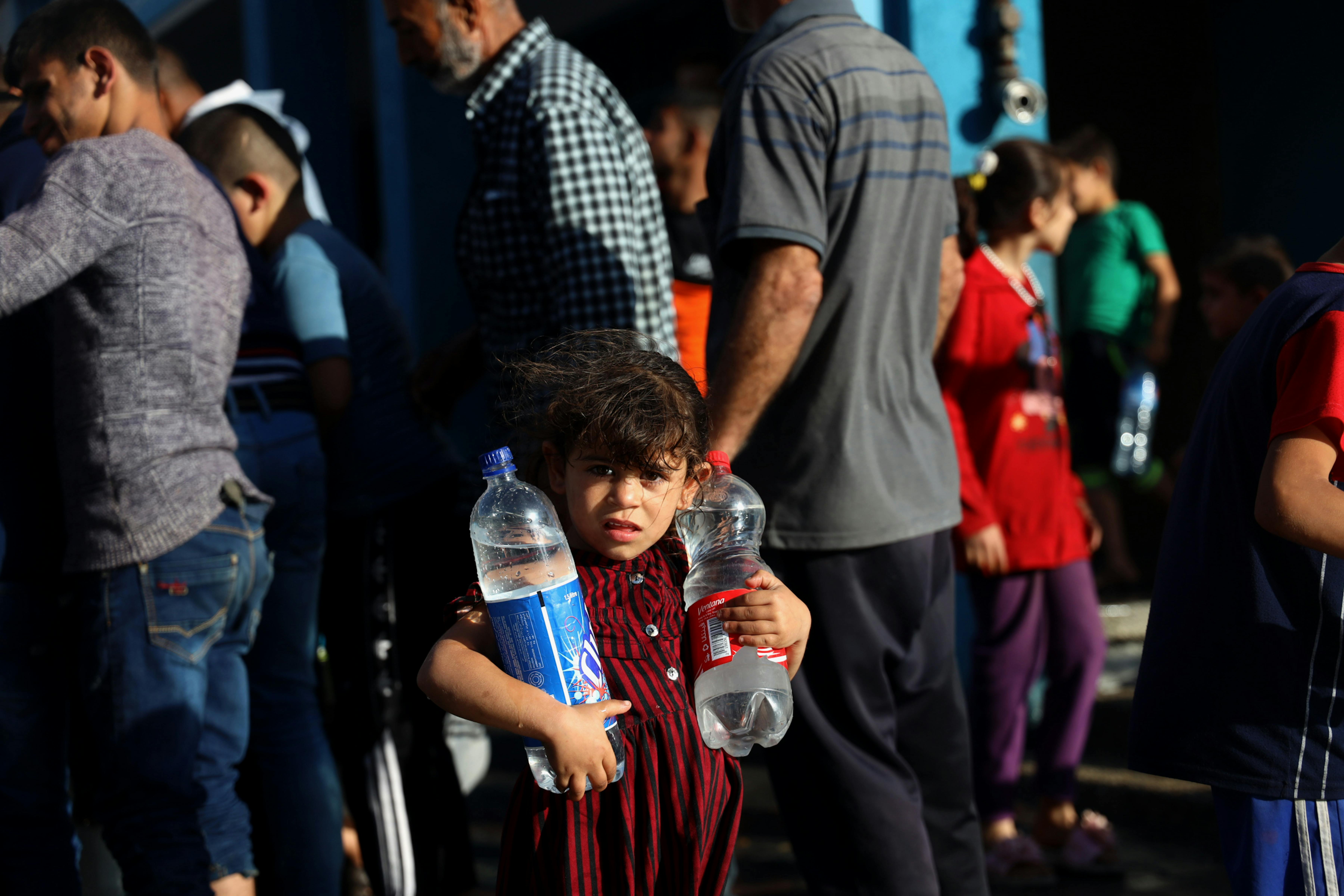 Una bambina palestinese trasporta due bottiglie d'acqua. I bombardamenti nella Striscia di Gaza del 2021 delhanno costretto centinaia di famiglie a fuggire dalle loro case nei rifugi scolastici dell'UNRWA.