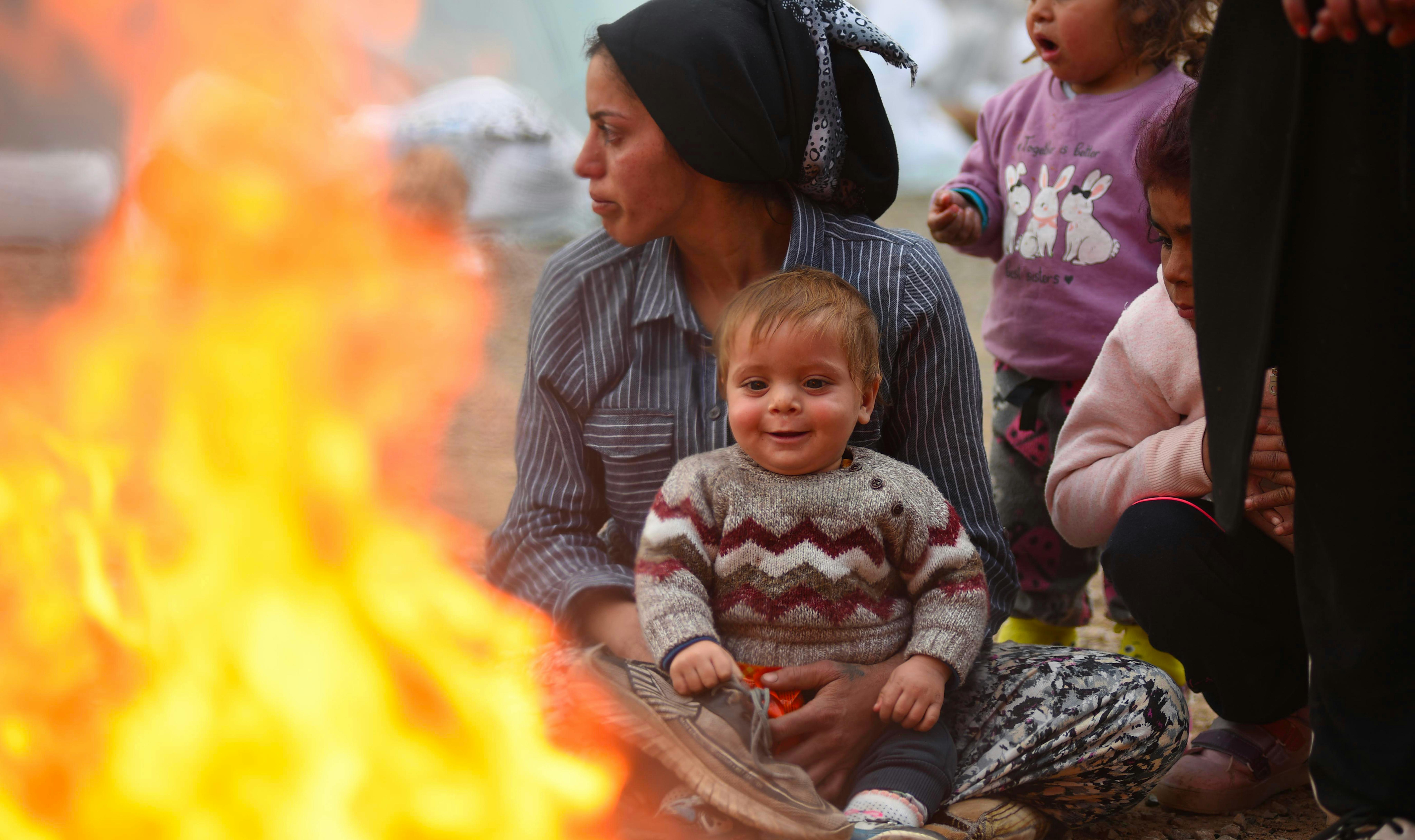 Terremoto Siria-Turchia: questo bambino sorride guardando il fuoco che riscalda lui e la sua famiglia nell'area di ricovero temporaneo composta da tende a Kahramanmaraş