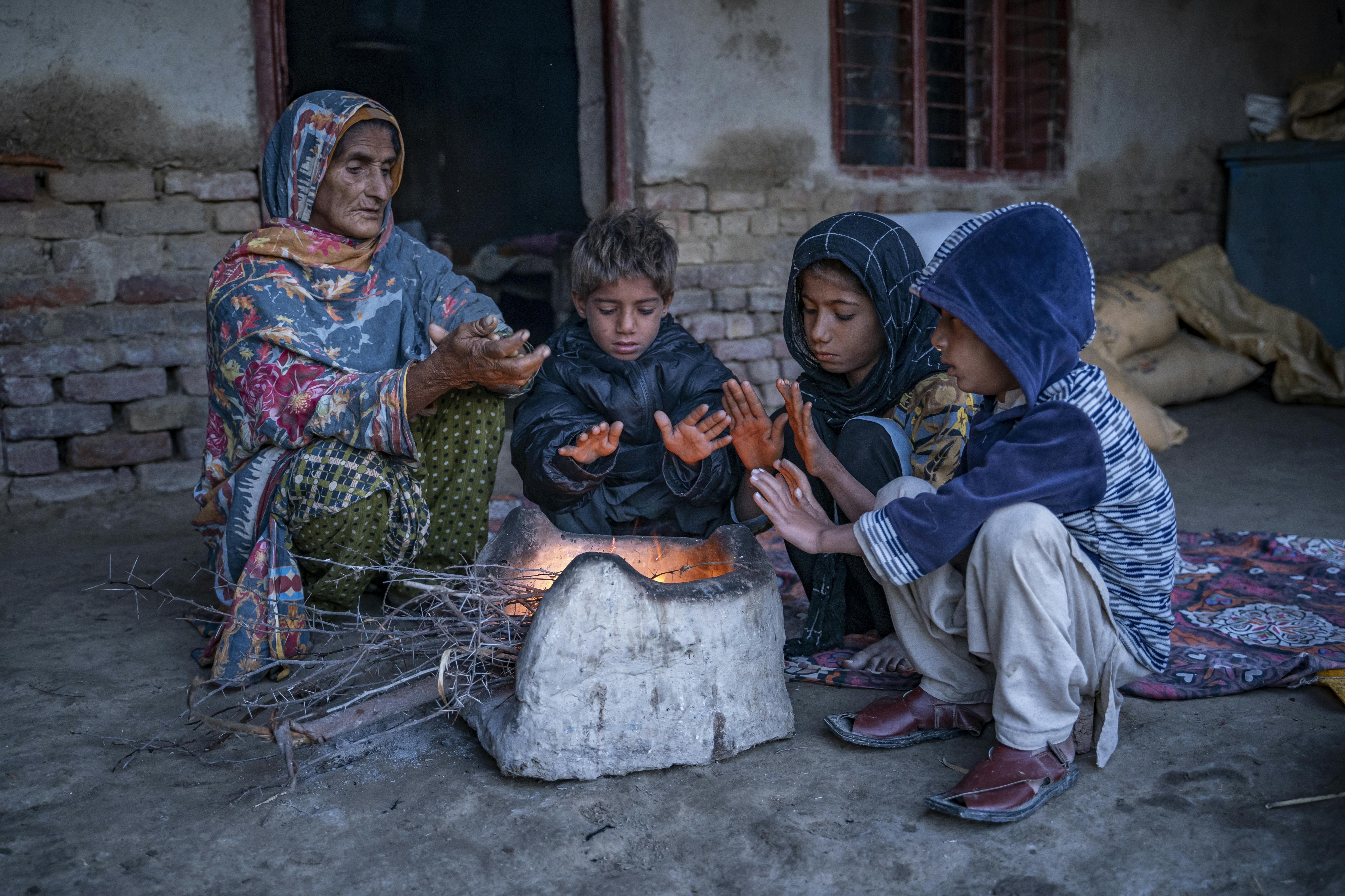 Hawa Bibi e i suoi nipoti si siedono attorno a una stufa nella loro casa per riscaldarsi nel villaggio di Zangi Brohi, distretto di Dadu, Sindh.